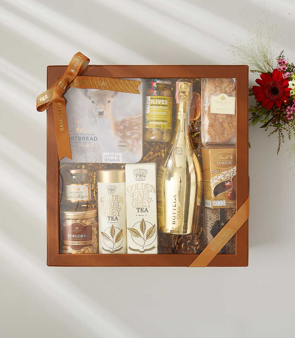 Gift box with champagne, gourmet tea, chocolates, shortbread, olives, and golden treats, perfect for elegant celebrations With a lid and beautifully tied with a bow.