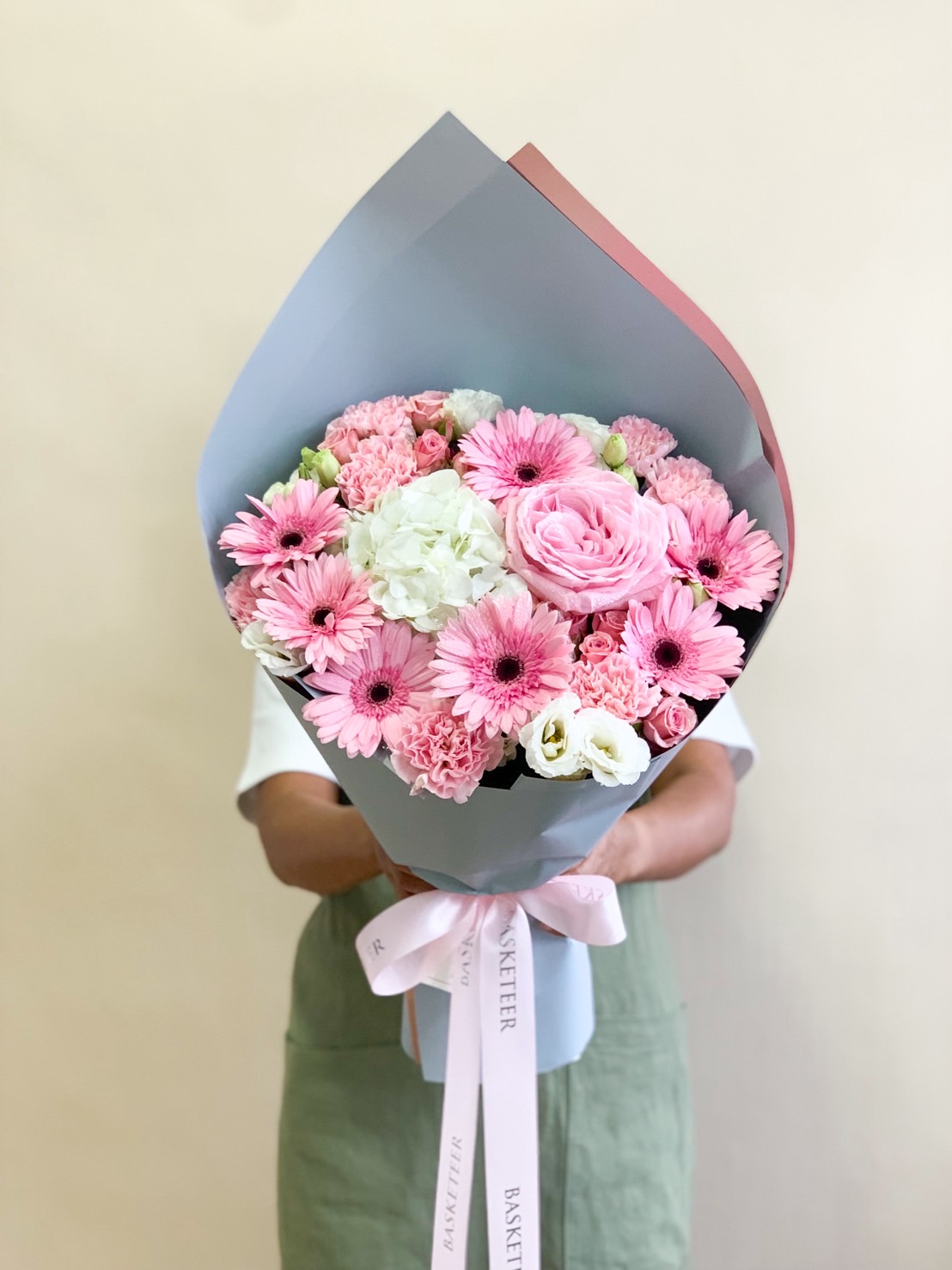 Elegant bouquet with pink gerbera daisies, pink roses, carnations, and white lisianthus wrapped in pastel paper with a pink ribbon.