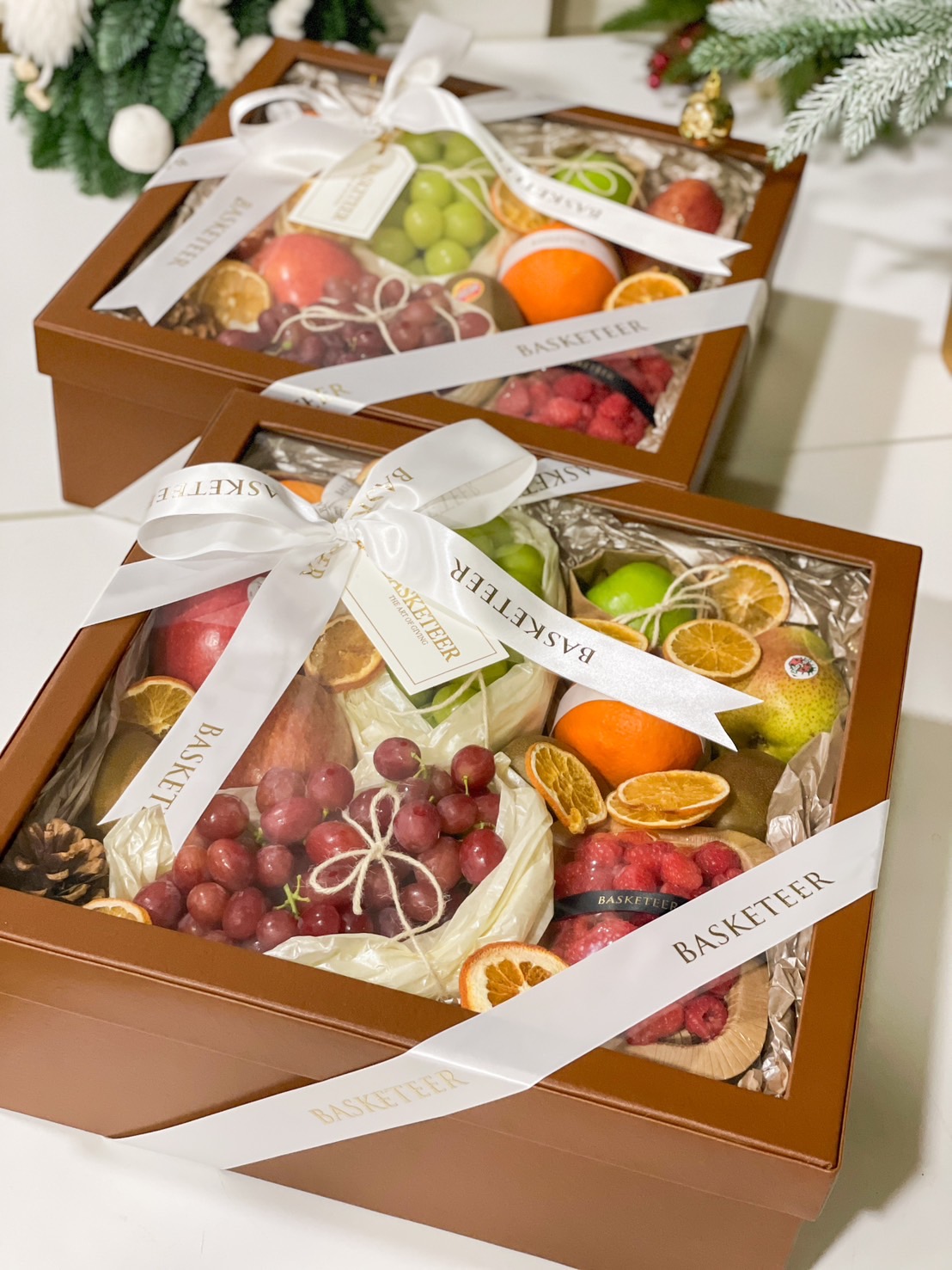 Luxurious fresh fruit gift box with apples, grapes, oranges, and berries, wrapped with a white Basketeer ribbon.