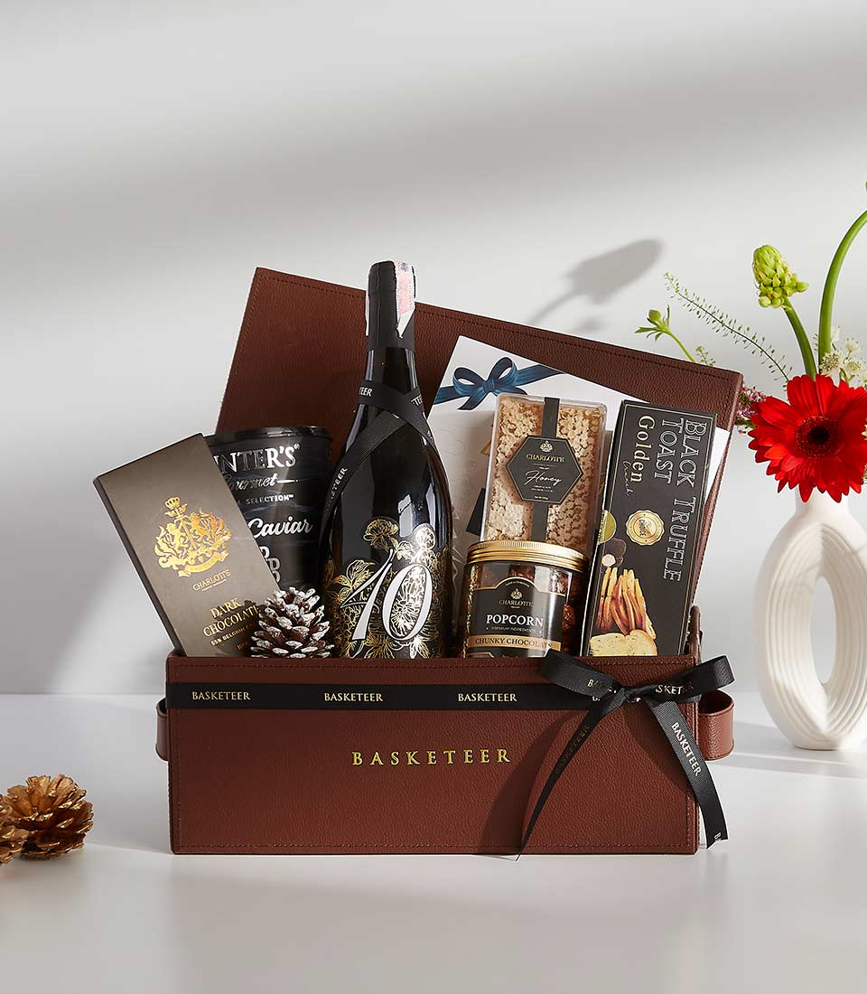 A brown leather gift box filled with various gourmet treats, including a bottle of champagne, caviar, chocolates, popcorn, and other snacks.