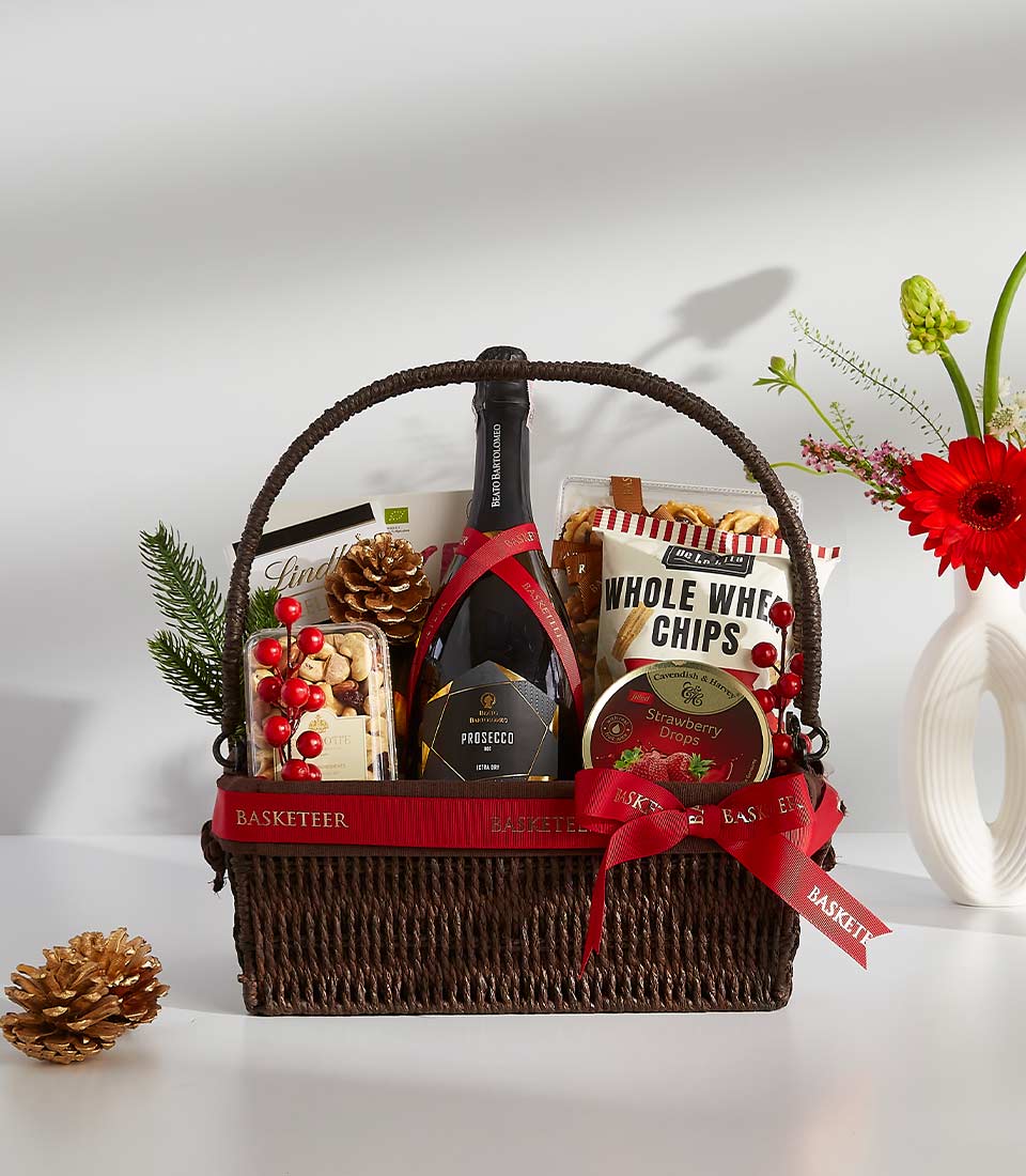 A brown wicker basket filled with a variety of gourmet treats, including a bottle of wine, chocolates