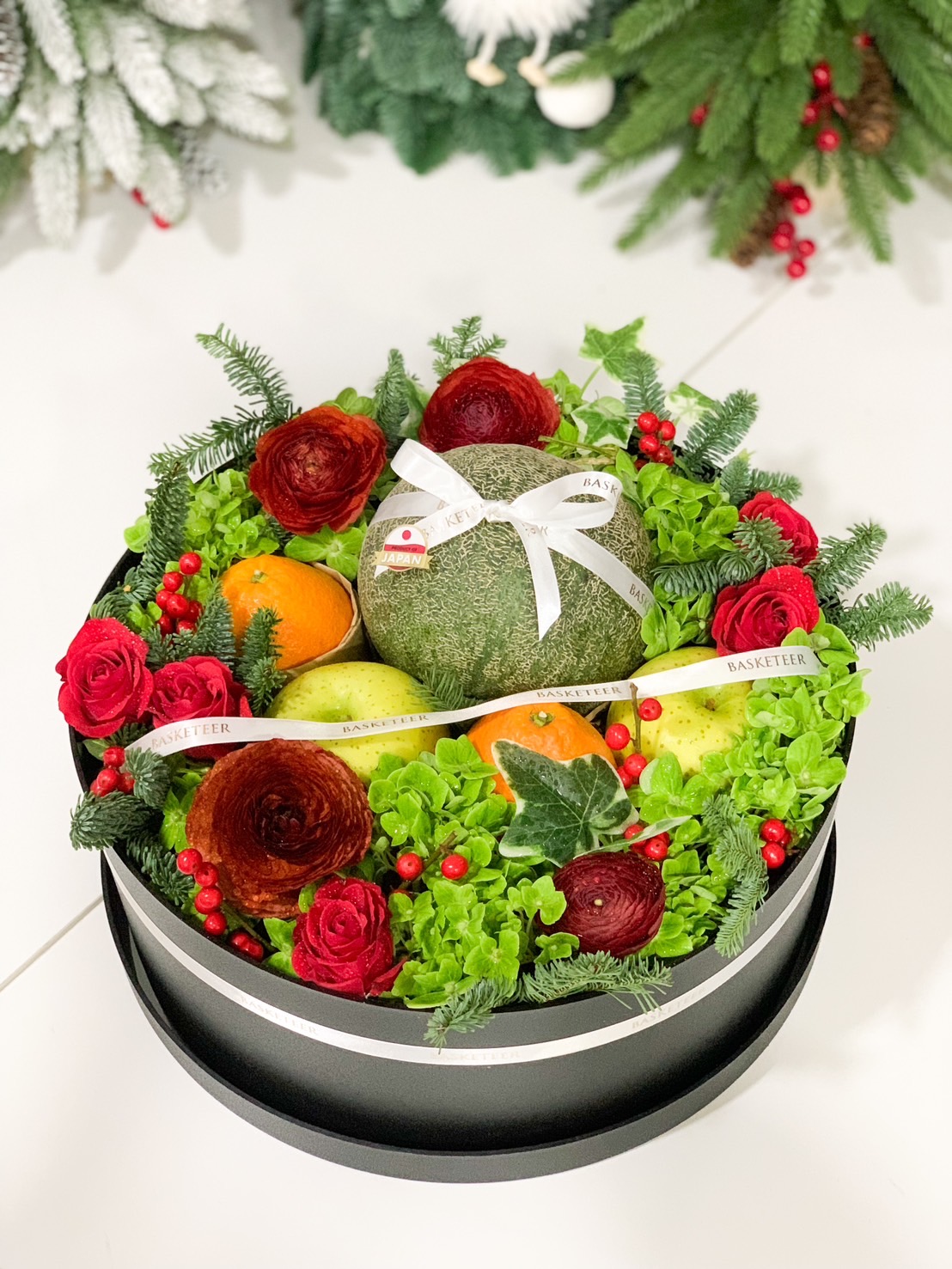 Luxury gift basket featuring a Japanese melon, citrus fruits, golden apples, and white florals, beautifully arranged for gifting.