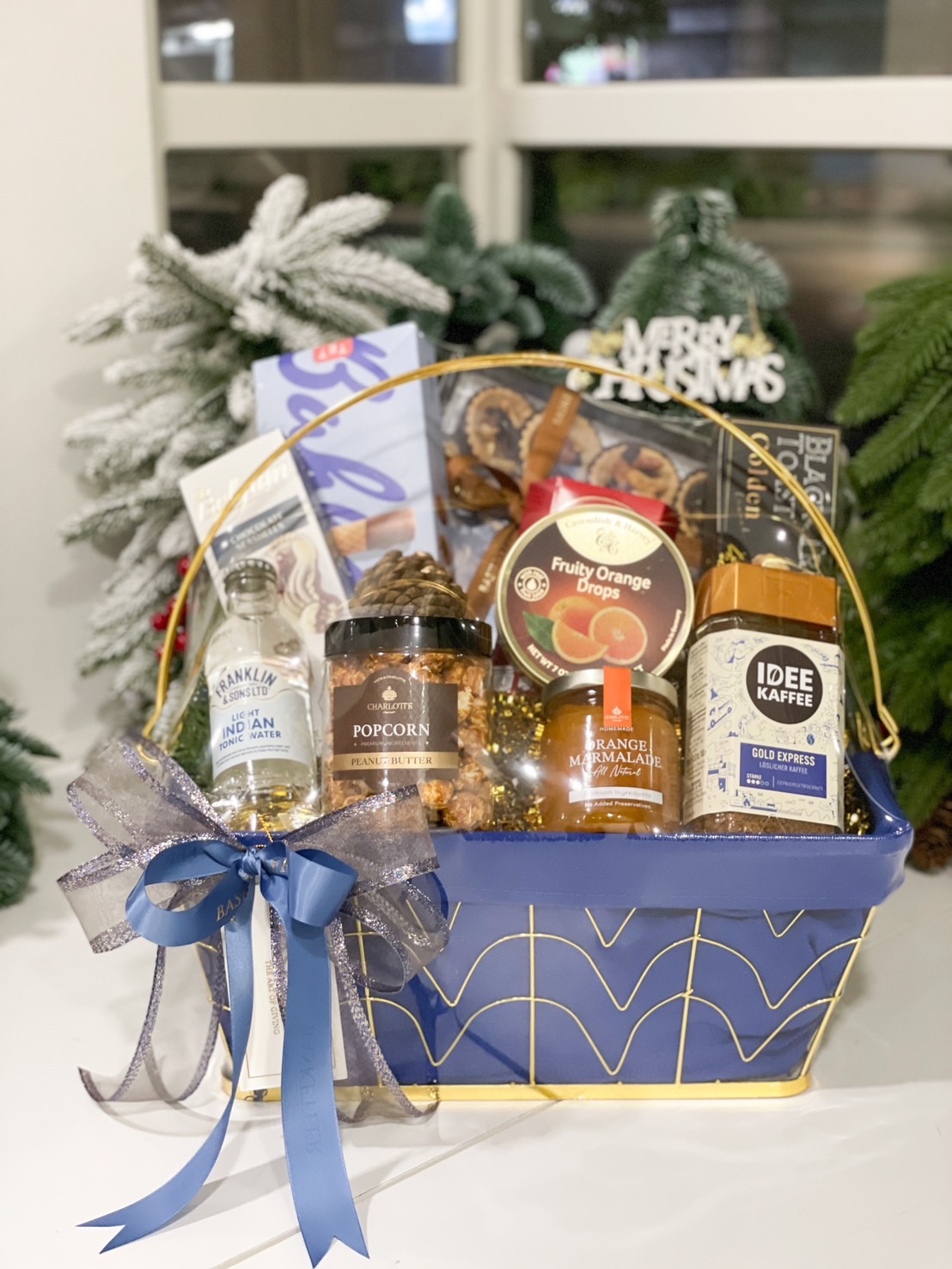 A luxurious blue gourmet gift basket with premium treats, including coffee, juice, and snacks, decorated with festive ribbons and pinecones.