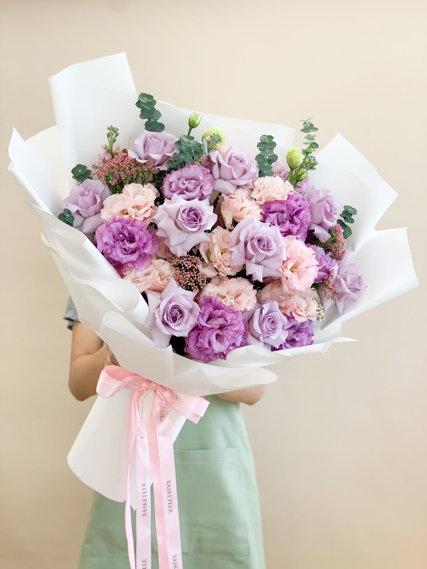 Lavender and pink floral bouquet with roses, lisianthus, and wildflowers wrapped in soft pink paper, tied with a ribbon.