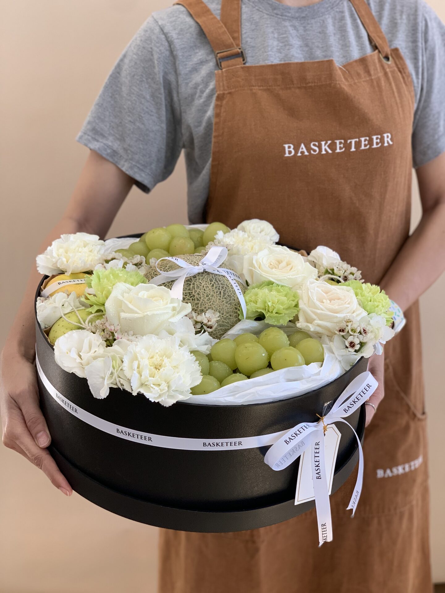 Premium Japanese fruit gift basket with melon, green grapes, golden apples, and white floral accents, beautifully styled for gifting.
