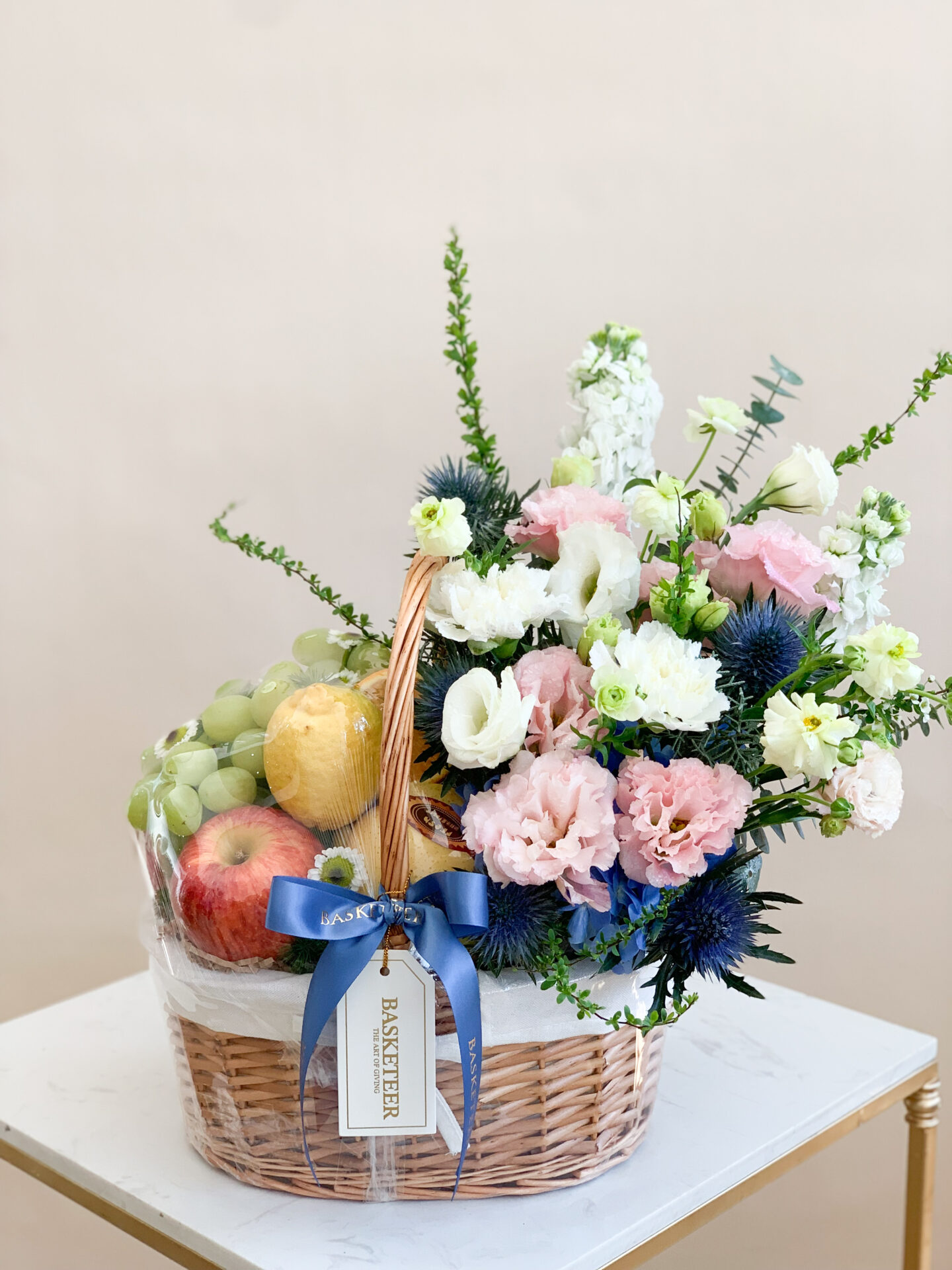 Pastel flower and fruit basket with fresh apples, grapes, pears, and a bouquet of pastel-colored flowers.