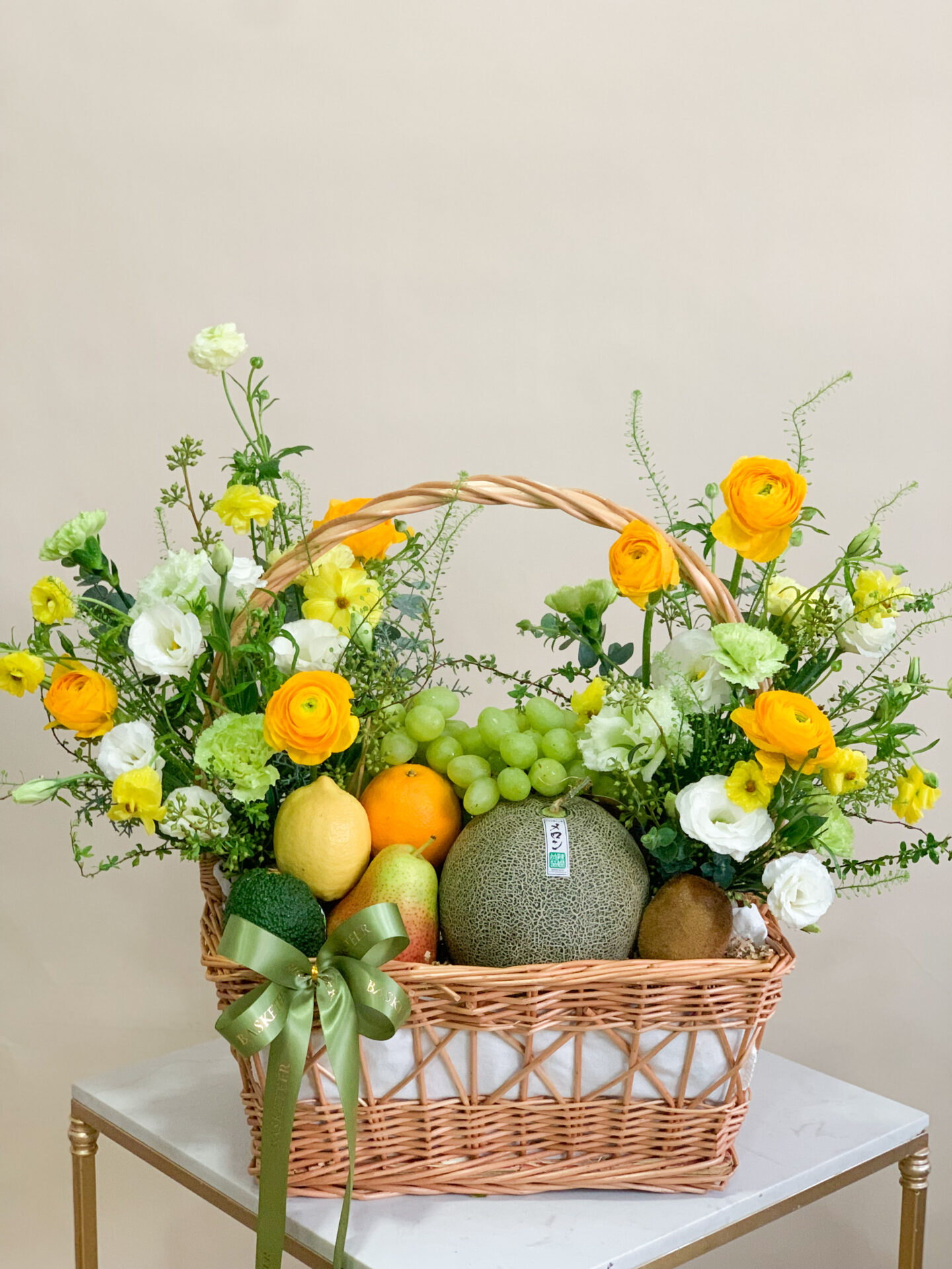 Sunshine fruit and flower basket with fresh melons, grapes, kiwi, citrus, and a bouquet of yellow and white flowers.