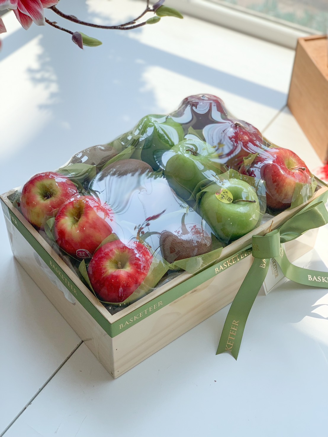 A premium wooden fruit gift box filled with fresh red apples, green apples, and kiwis, wrapped with a green ribbon.
