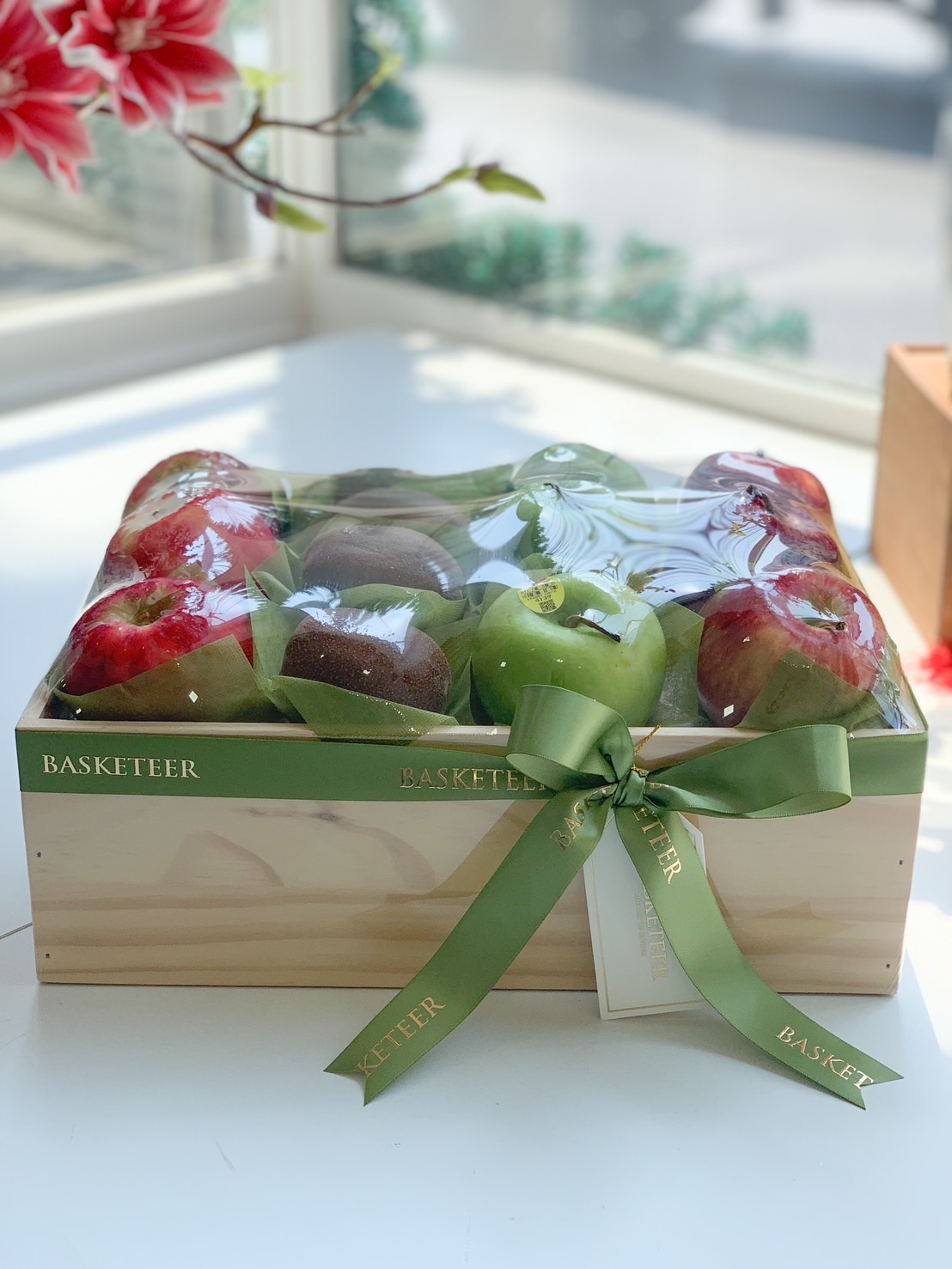 A premium wooden fruit gift box filled with fresh red apples, green apples, and kiwis, wrapped with a green ribbon.