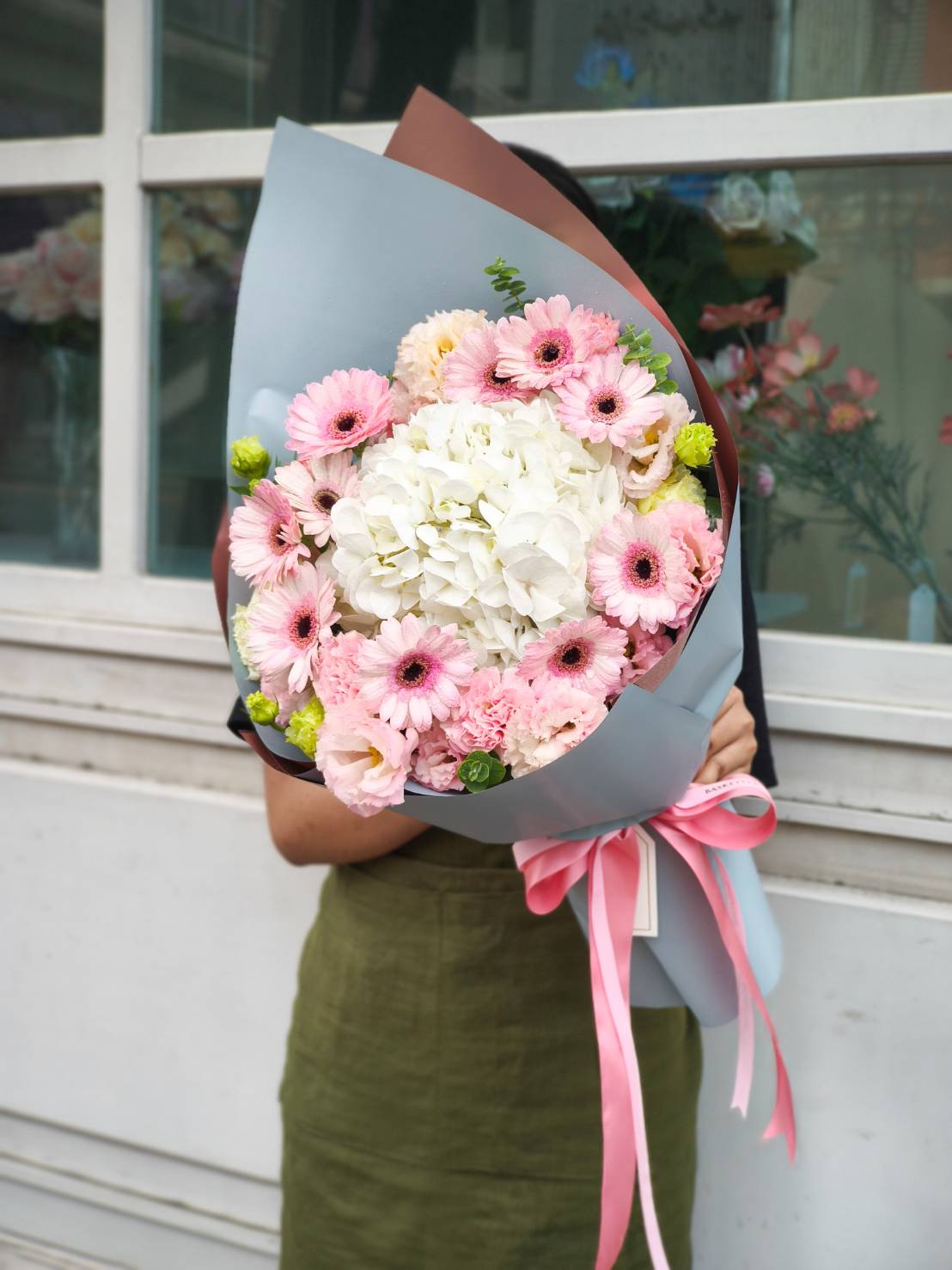 Hand-tied bouquet with pink gerbera daisies, white hydrangea, soft pink lisianthus, and green accents.