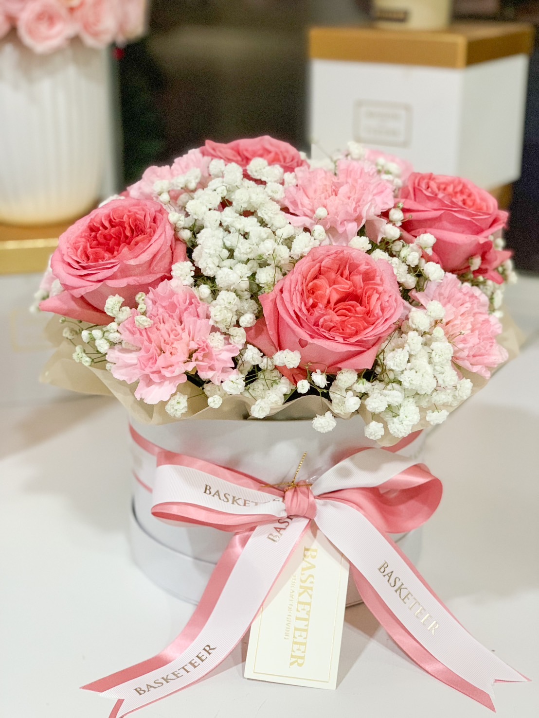 A luxury pink rose floral box featuring romantic pink garden roses, soft carnations, and delicate baby’s breath, elegantly tied with a pink and white ribbon.