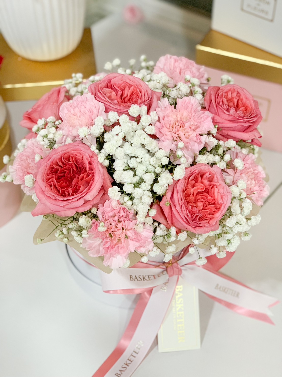 A luxury pink rose floral box featuring romantic pink garden roses, soft carnations, and delicate baby’s breath, elegantly tied with a pink and white ribbon.