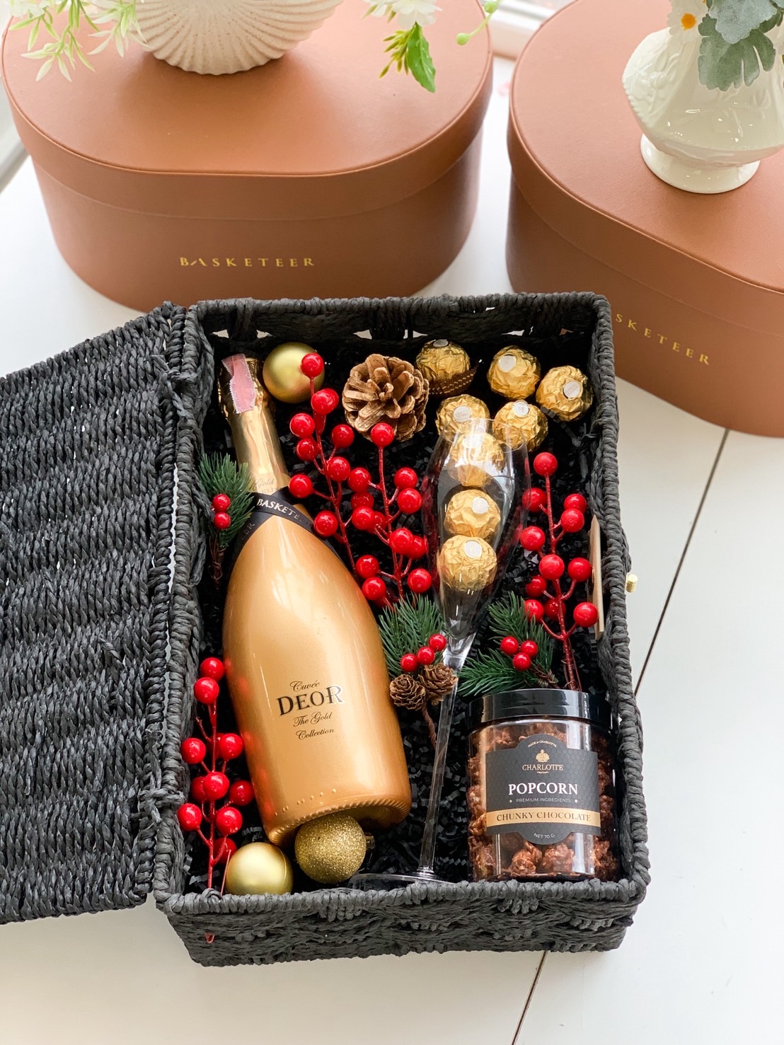 Black basket filled with golden sparkling wine, Ferrero Rocher, chocolate popcorn and champagne flute, holiday-themed decor