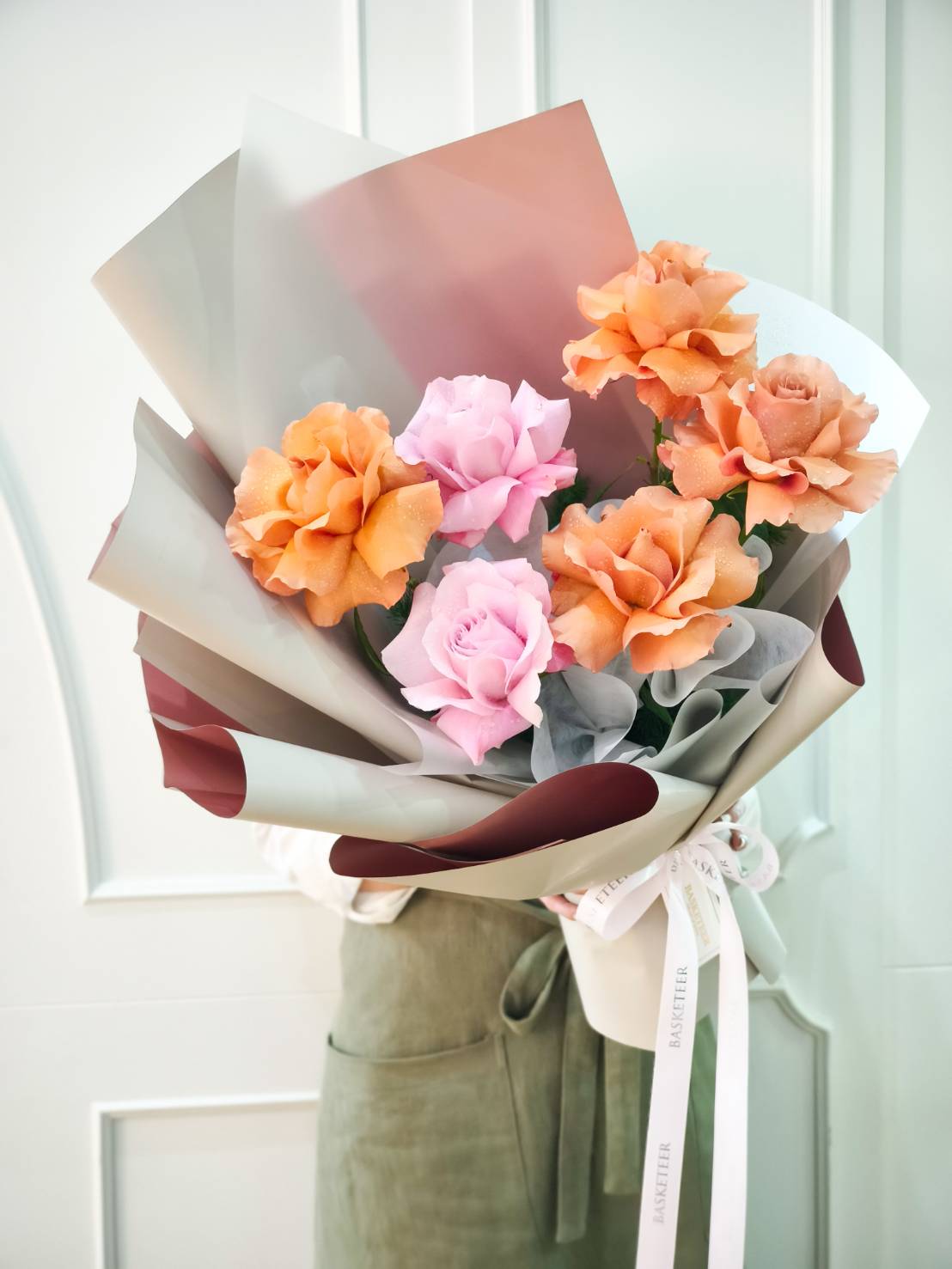Bouquet of caramel orange roses and blush pink roses wrapped in elegant paper with satin ribbon.