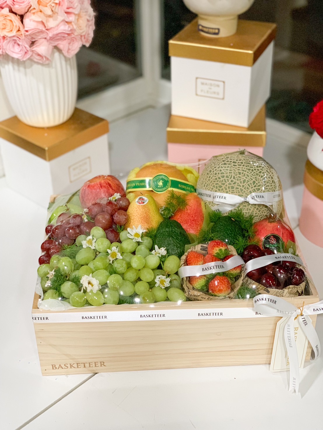 A luxury fresh fruit basket filled with premium imported grapes, apples, pears, melon, strawberries, and cherries, elegantly arranged in a wooden crate with Basketeer’s signature ribbon. Perfect for gifting.