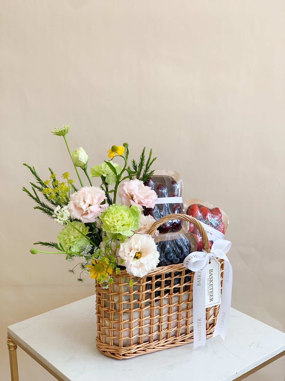 A beautifully curated fresh fruit and floral basket featuring premium cherries, strawberries, blueberries, and fresh flowers in a handwoven rattan basket. The perfect gift for any occasion!