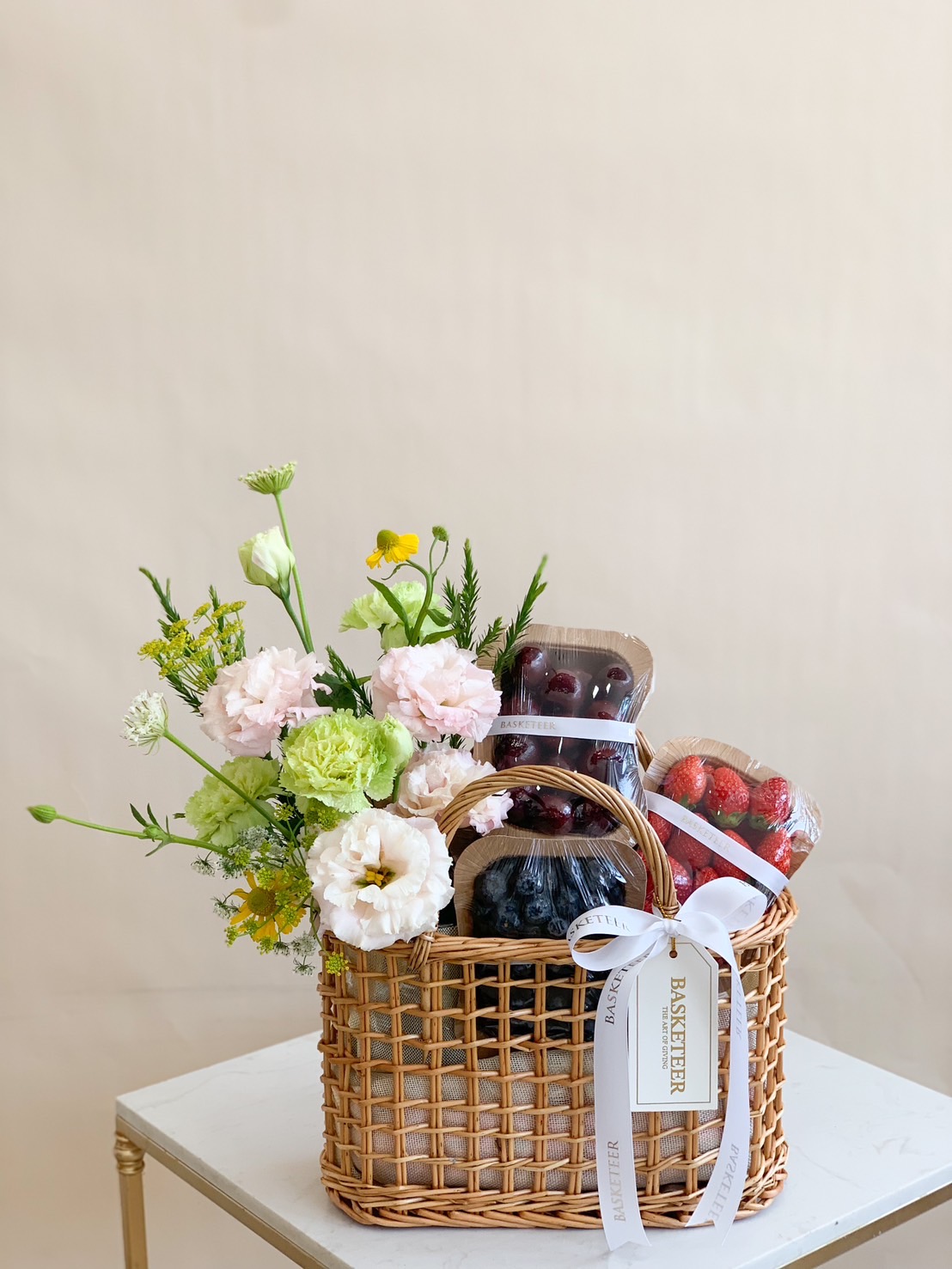 A beautifully curated fresh fruit and floral basket featuring premium cherries, strawberries, blueberries, and fresh flowers in a handwoven rattan basket. The perfect gift for any occasion!