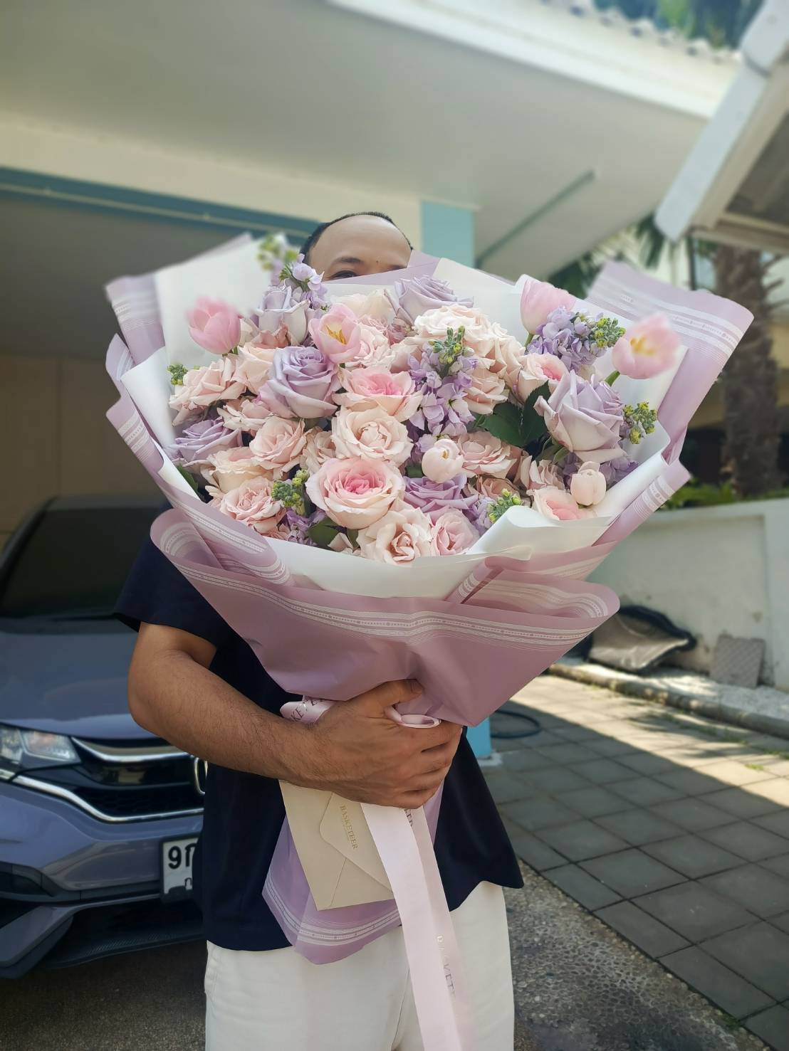 A luxurious lavender and pastel pink flower bouquet featuring roses, tulips, and lush blooms, elegantly wrapped in soft lilac paper with a ribbon, perfect for gifting.