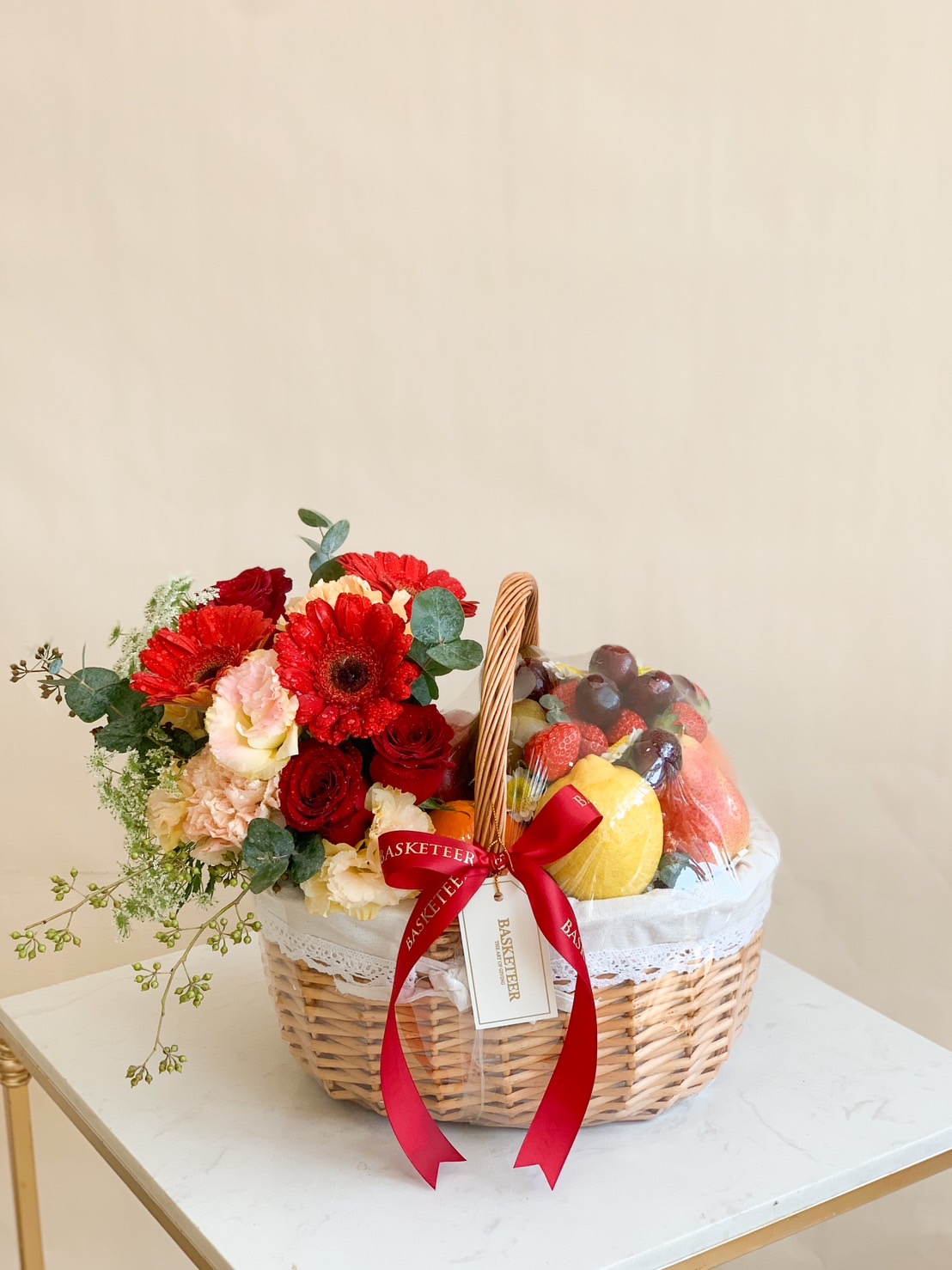 A beautifully arranged premium fresh fruit and floral basket featuring apples, grapes, oranges, strawberries, and citrus fruits, elegantly wrapped and decorated with luxurious red roses, carnations, and gerbera daisies. Perfect for birthdays, celebrations, get-well wishes, and corporate gifts.