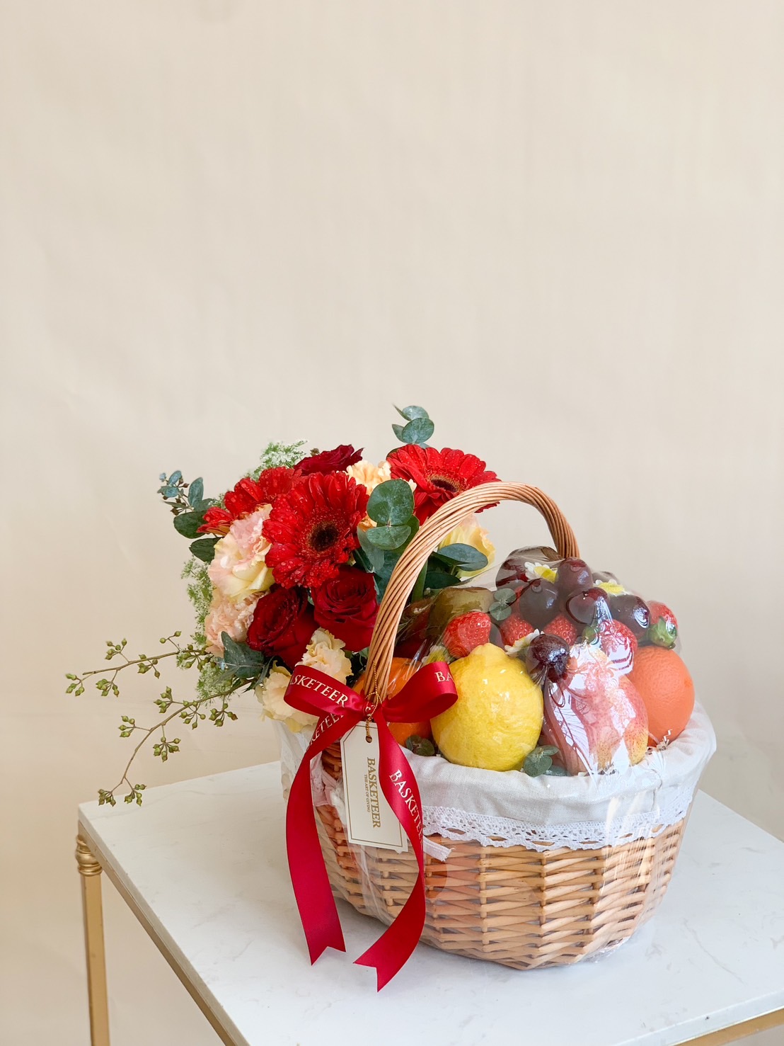 A beautifully arranged premium fresh fruit and floral basket featuring apples, grapes, oranges, strawberries, and citrus fruits, elegantly wrapped and decorated with luxurious red roses, carnations, and gerbera daisies. Perfect for birthdays, celebrations, get-well wishes, and corporate gifts.