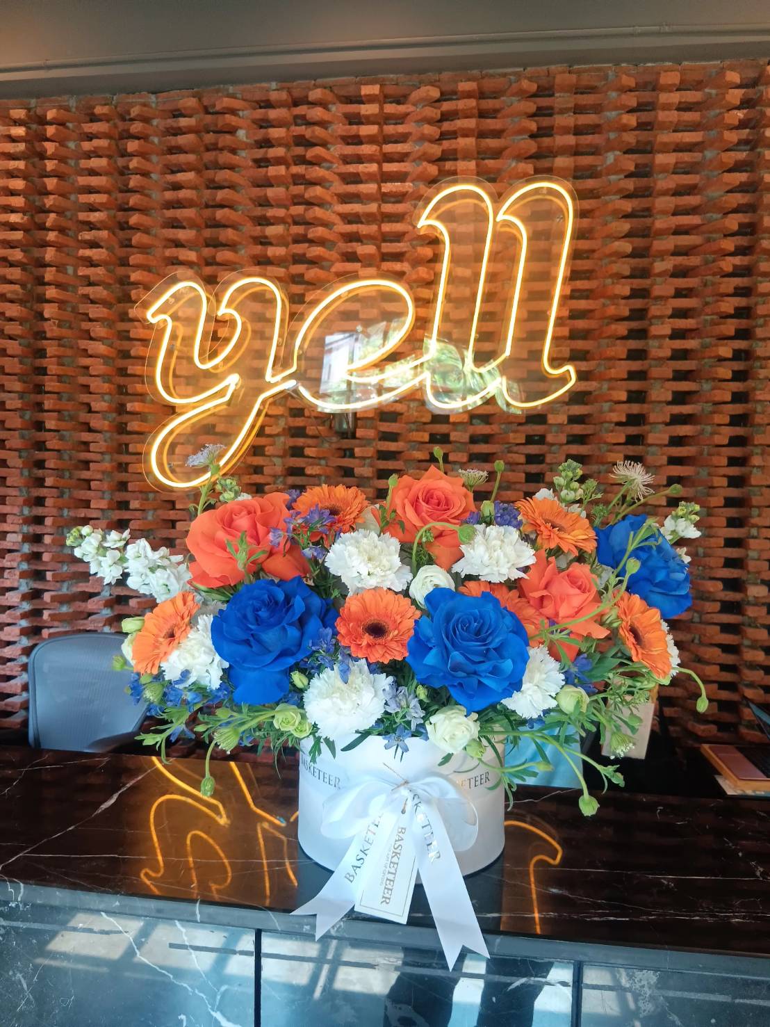 A stunning blue and orange floral arrangement in a white round box with premium roses, gerberas, and lush greenery – perfect for corporate gifts and grand openings.
