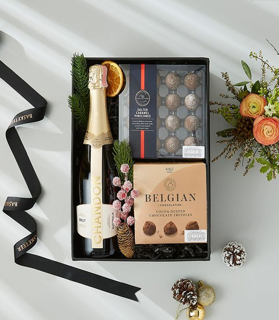 A festive Christmas gift box, adorned with a vibrant red satin ribbon, overflowing with luxurious treats and sparkling wine