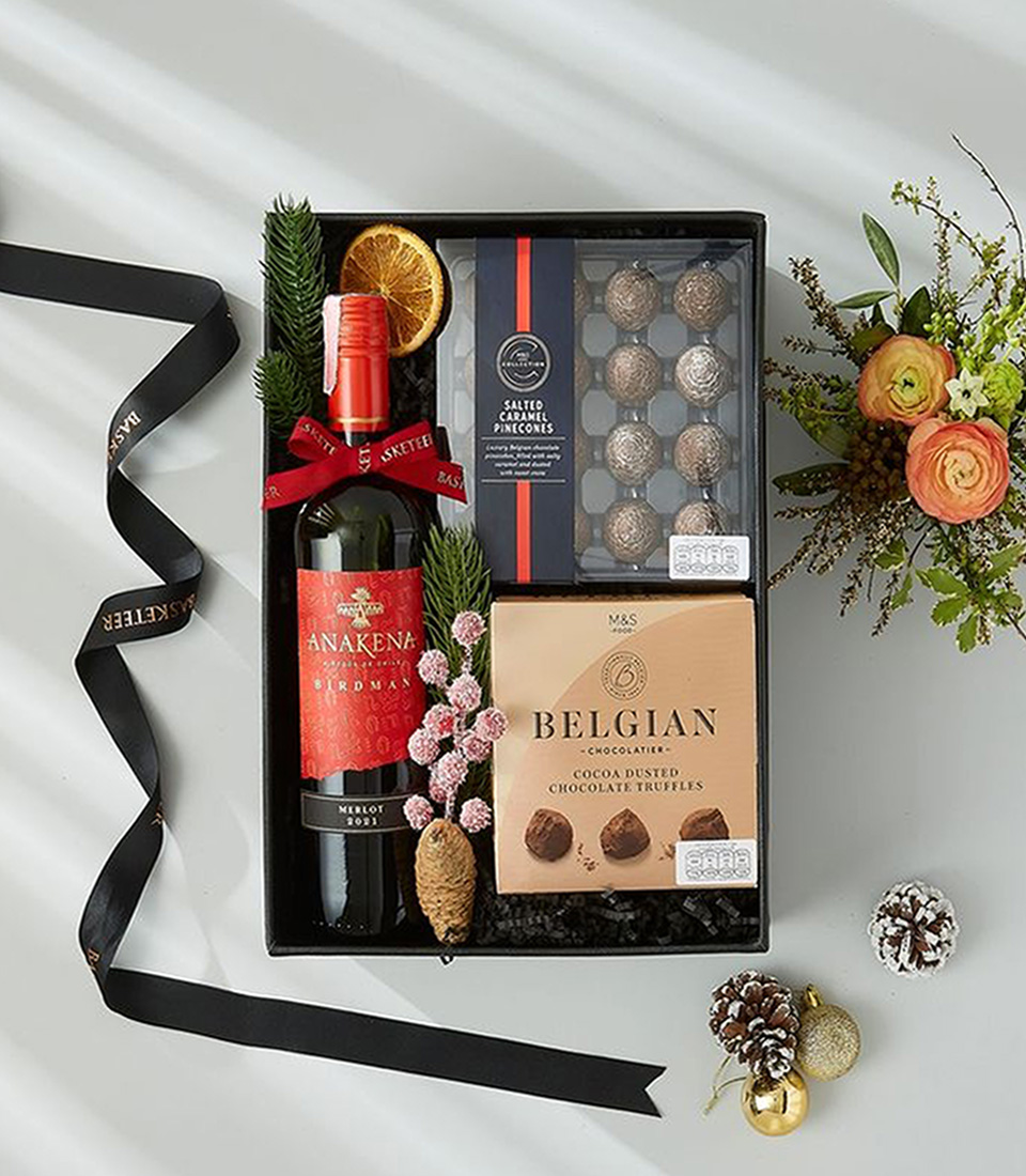 A festive Christmas gift box, adorned with a vibrant red satin ribbon, overflowing with luxurious treats and Red wine