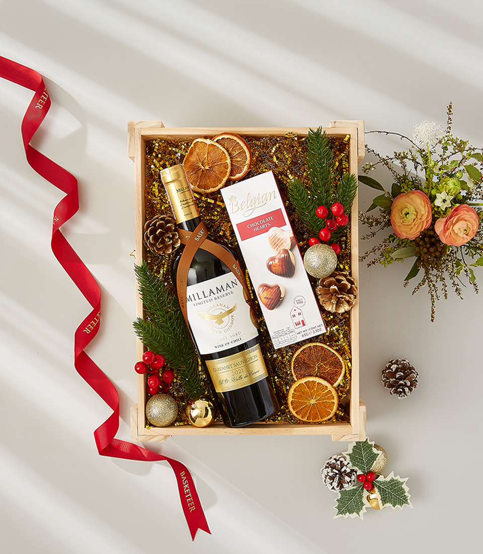 A festive gift box overflowing with holiday goodies, including a bottle of Cabernet Sauvignon, gourmet chocolates, and seasonal ornaments.
