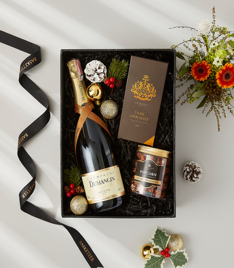 A black gift box with a gold ribbon, containing a bottle of champagne, a box of chocolate, and a jar of popcorn