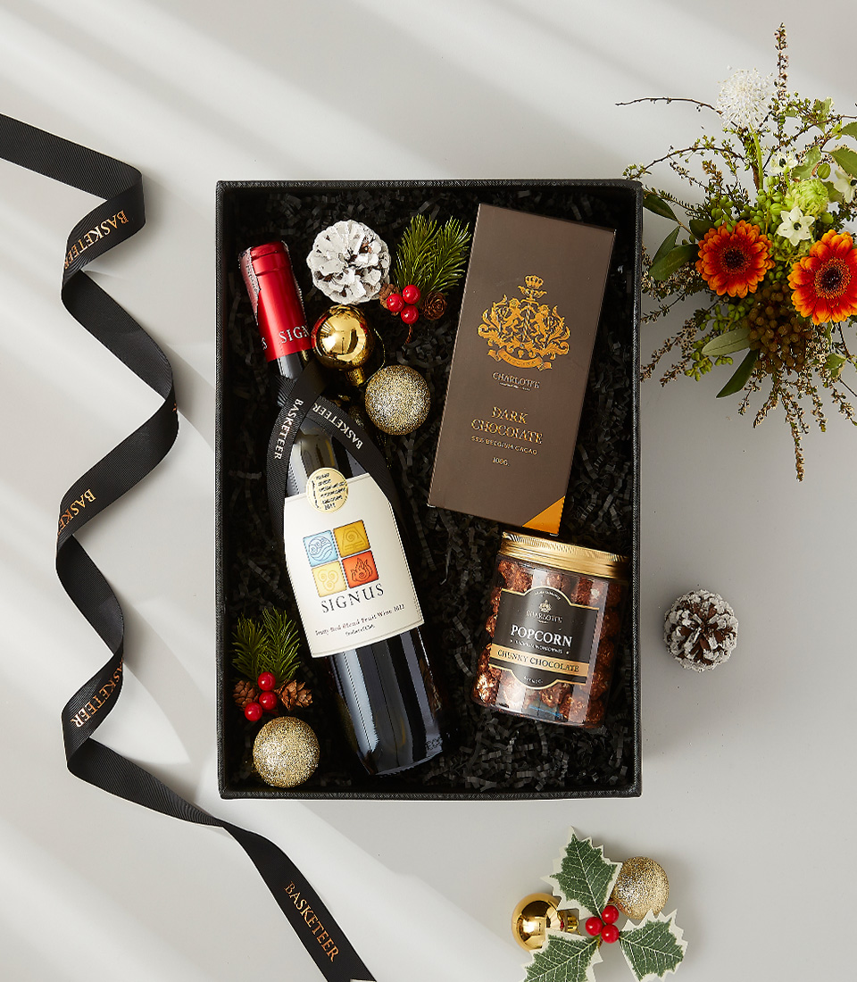 A festive gift box overflowing with holiday goodies, including a bottle of Appassimento wine, gourmet chocolate, and seasonal ornaments.