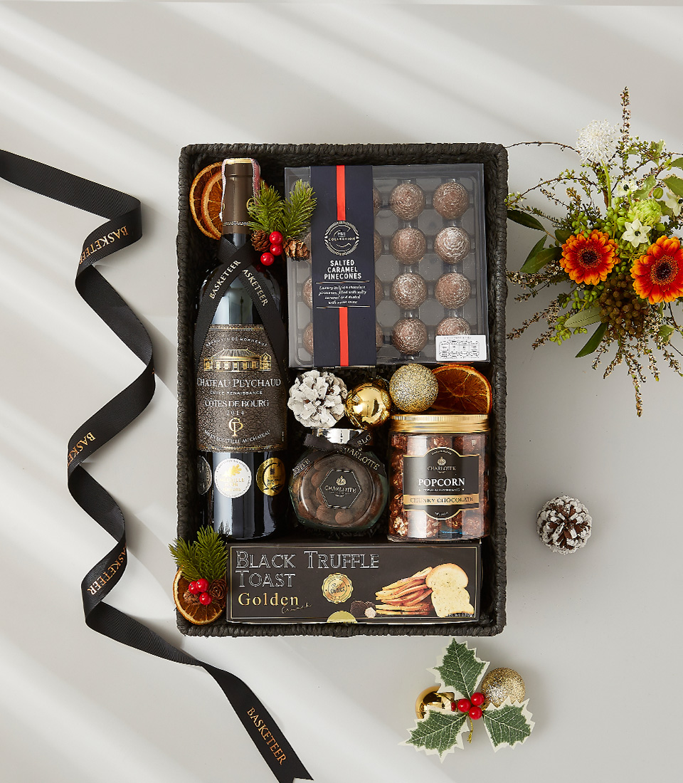 A festive gift box overflowing with holiday goodies, including a bottle of Appassimento wine, gourmet chocolate, and seasonal ornaments.