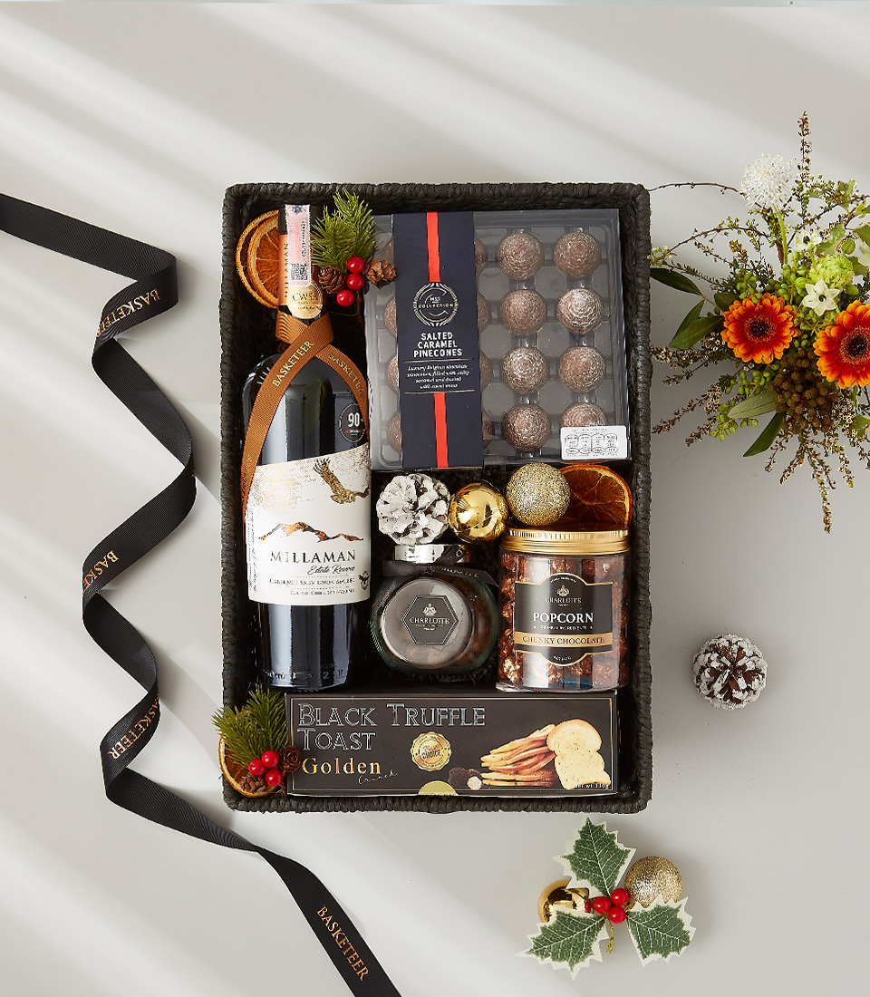 A festive gift box overflowing with holiday goodies, including a bottle of Appassimento wine, gourmet chocolate, and seasonal ornaments.