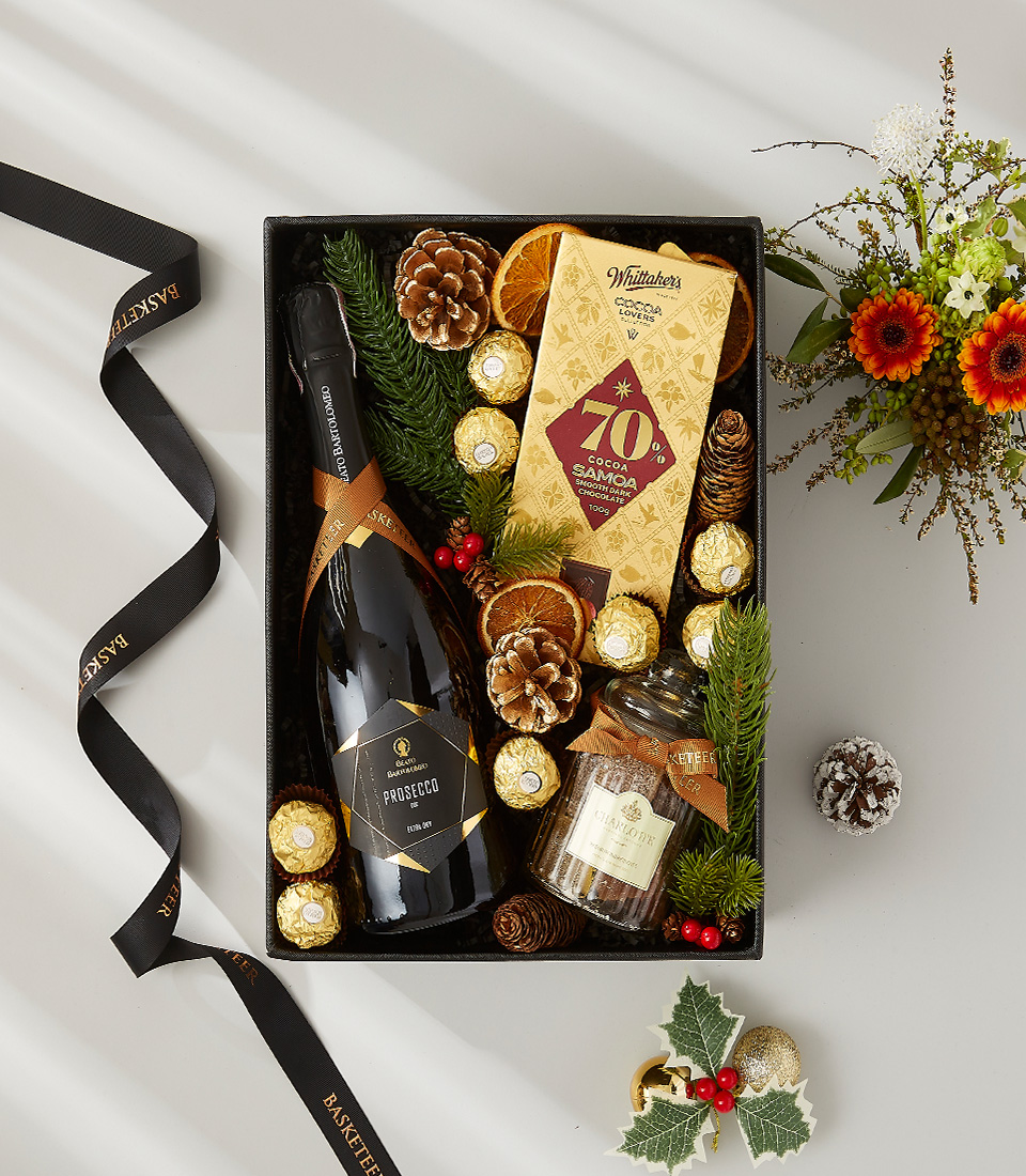 Festive gift box containing a bottle of prosecco, gourmet chocolate truffles, and scented candles. Decorated with pine cones, dried oranges, and holly.