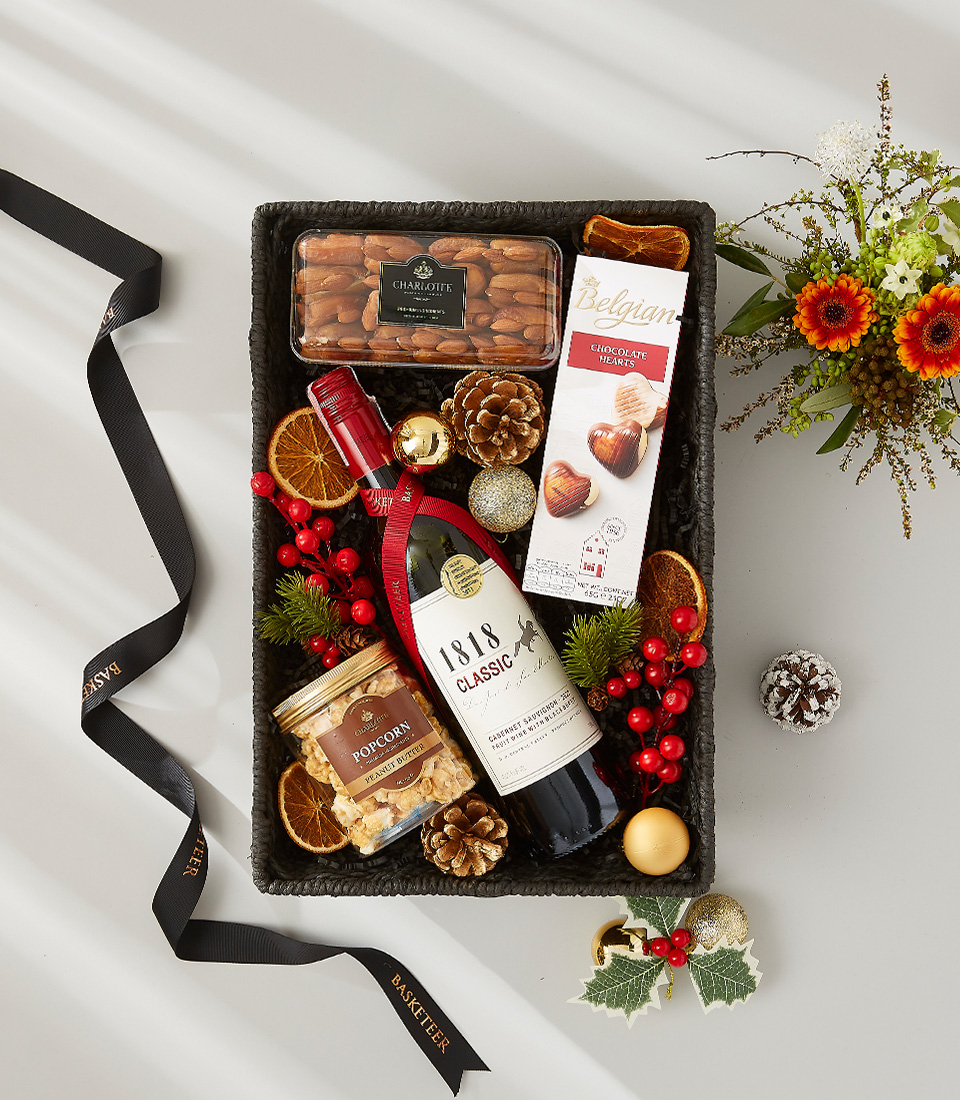 A luxurious holiday gift basket filled with a bottle of red wine, a selection of gourmet snacks, and festive decorations.