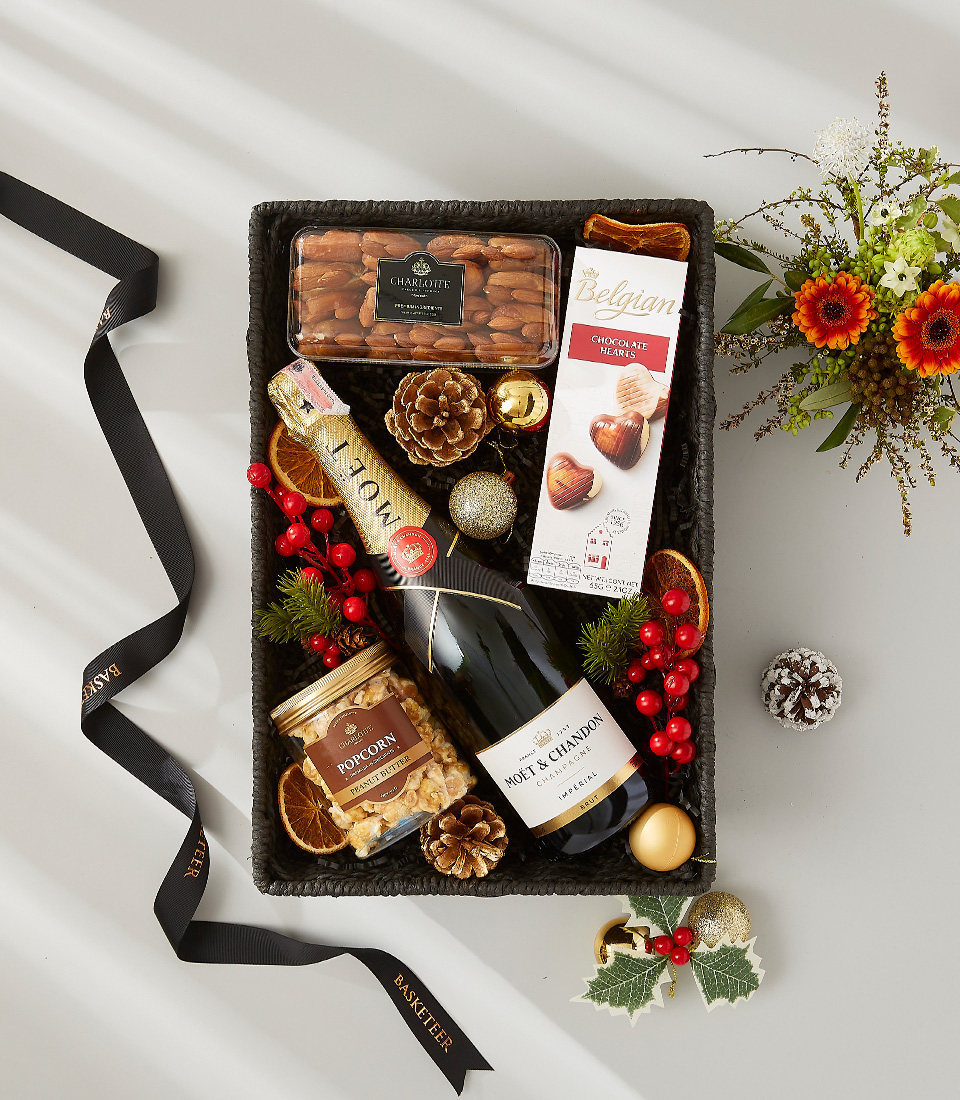 A luxurious holiday gift basket filled with a bottle of golden champagne, a selection of gourmet snacks, and festive decorations.