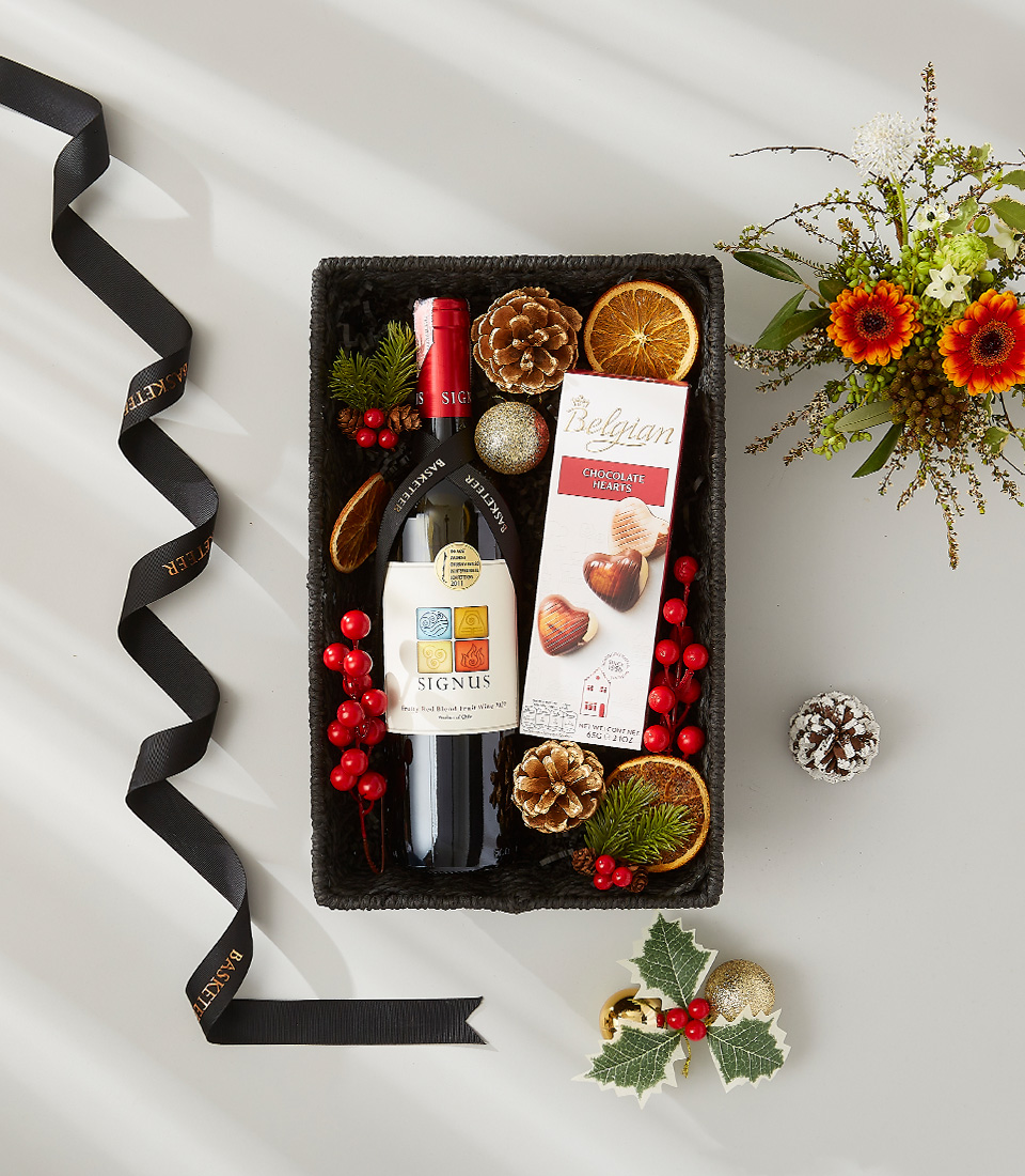 A luxurious holiday gift basket filled with a bottle of red wine, a selection of gourmet snacks, and festive decorations.