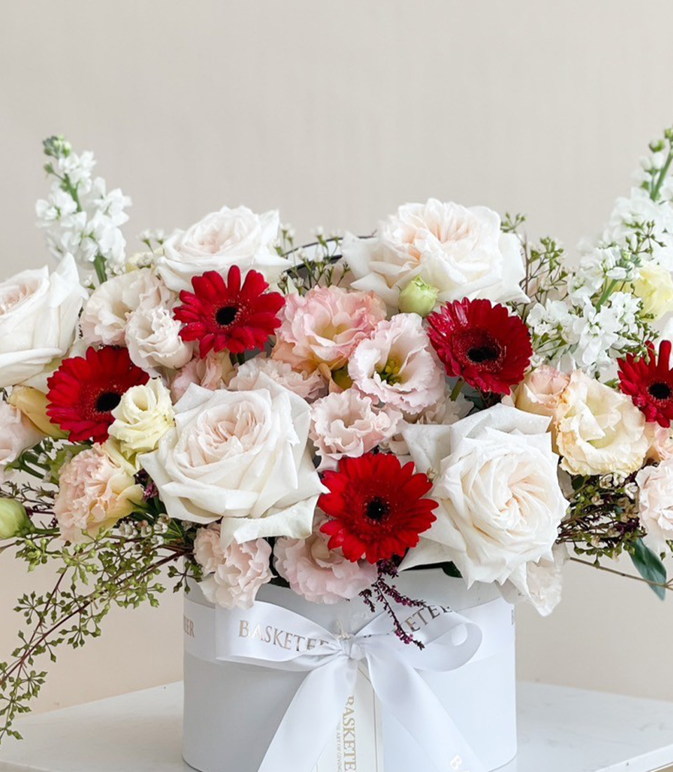Elegant flower box with white roses, red gerberas, and pastel pink blooms arranged in a white container with a ribbon.