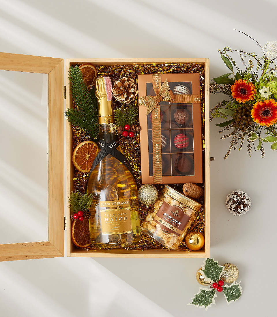 A luxurious holiday gift basket filled with a bottle of champagne, a selection of gourmet snacks, and festive decorations.