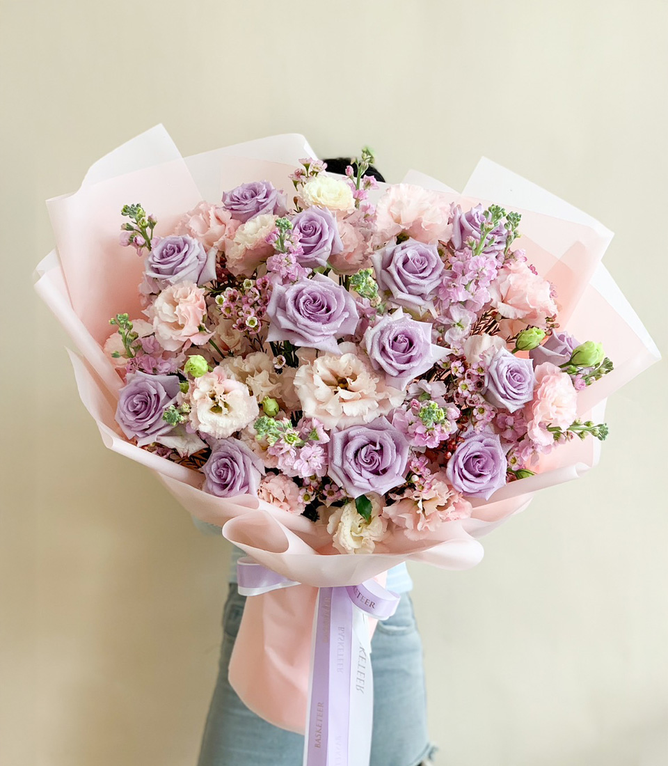 Lavender and pink floral bouquet with roses, lisianthus, and wildflowers wrapped in soft pink paper, tied with a ribbon.