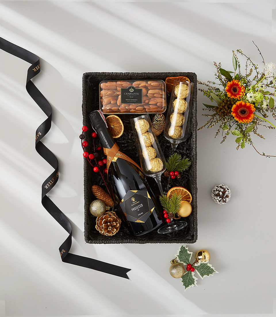 A luxurious holiday gift basket filled with a bottle of Prosecco, a selection of gourmet snacks, and festive decorations.
