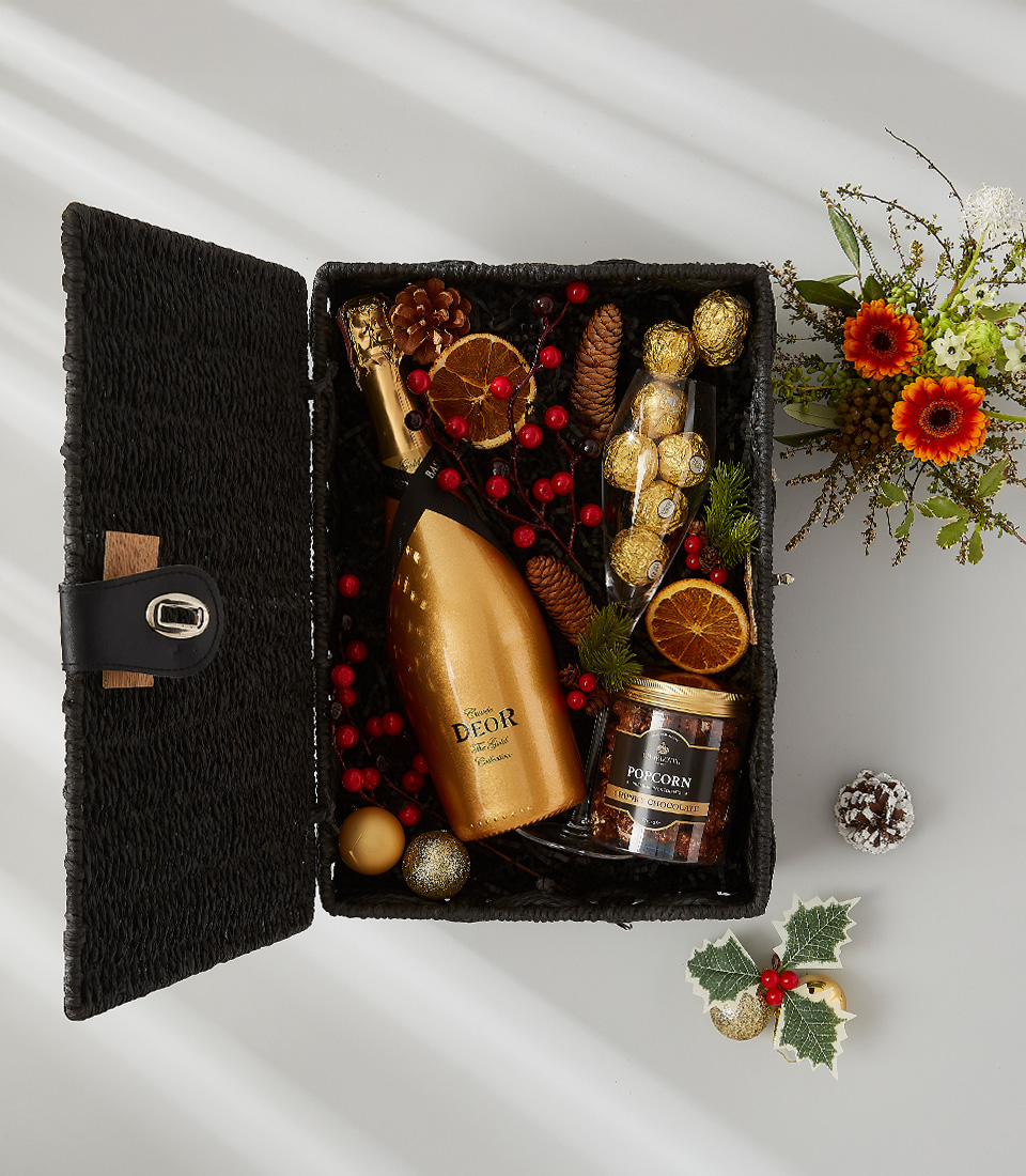 A luxurious holiday gift basket filled with a bottle of Deor Gold, a selection of gourmet snacks, and festive decorations.