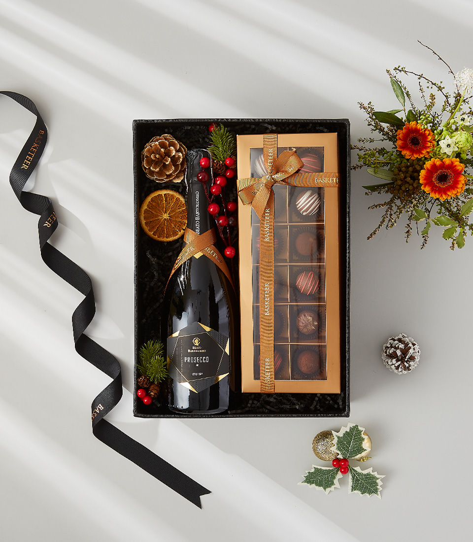 A beautifully wrapped gift box filled with a bottle of Prosecco, a box of gourmet chocolates, and festive decorations. Perfect for any occasion.