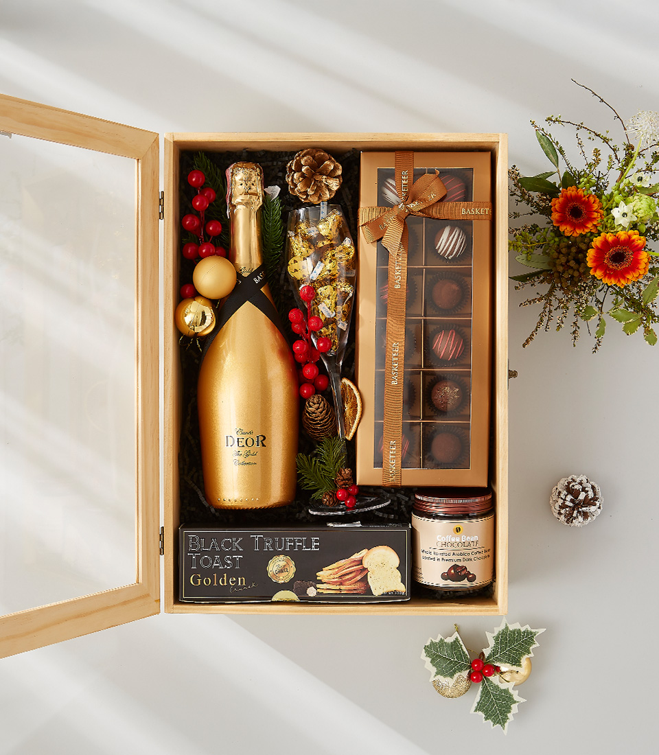 Festive gift box containing a golden bottle of champagne, gourmet snacks, and holiday decorations.