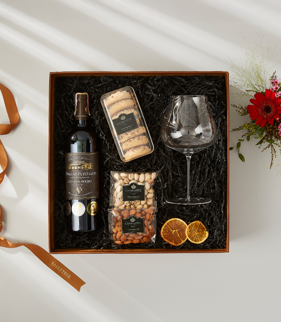 Château Peychaud wine gift set with gourmet snacks, nuts, cookies, and a wine glass.