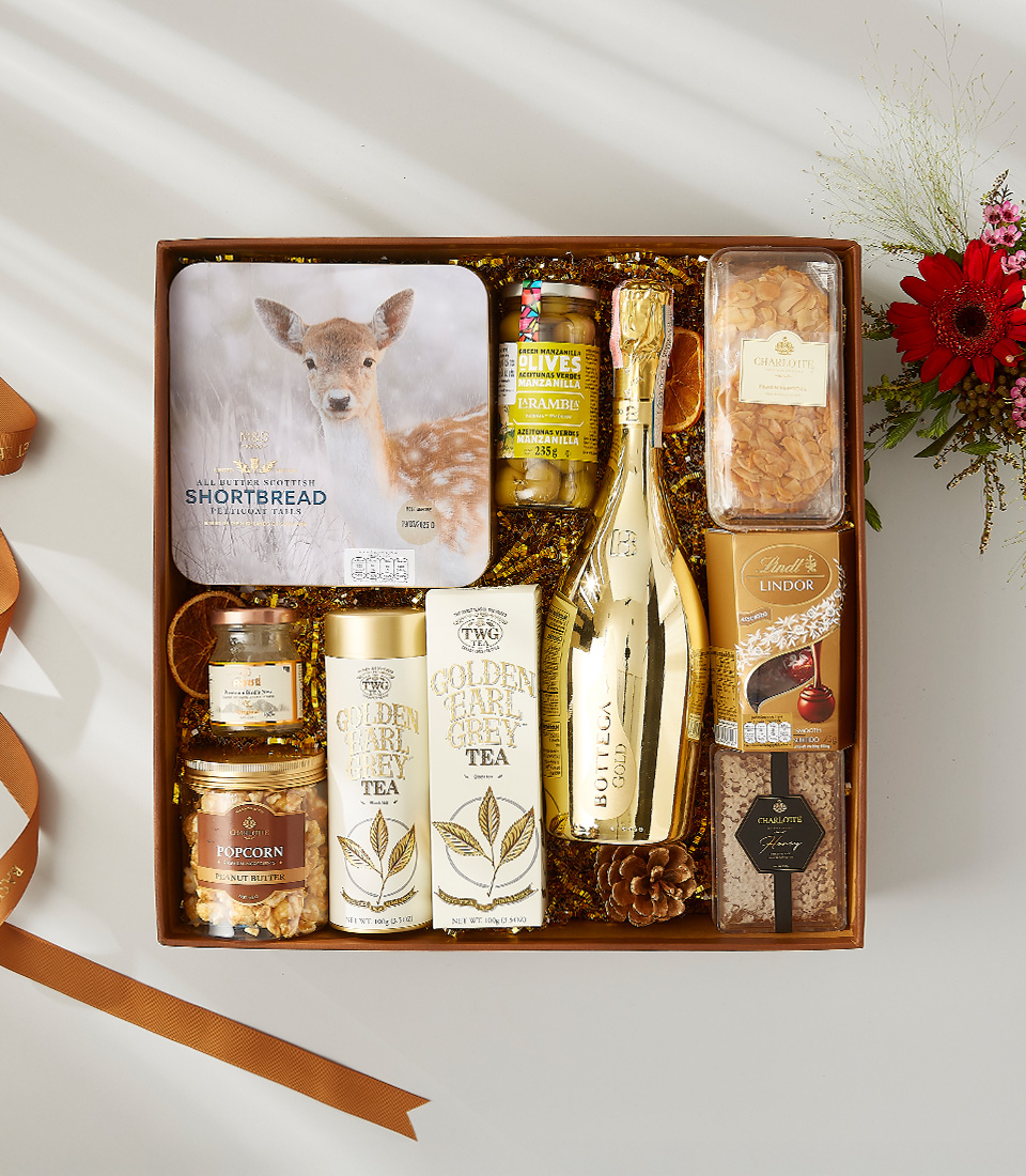 Gift box with champagne, gourmet tea, chocolates, shortbread, olives, and golden treats, perfect for elegant celebrations.