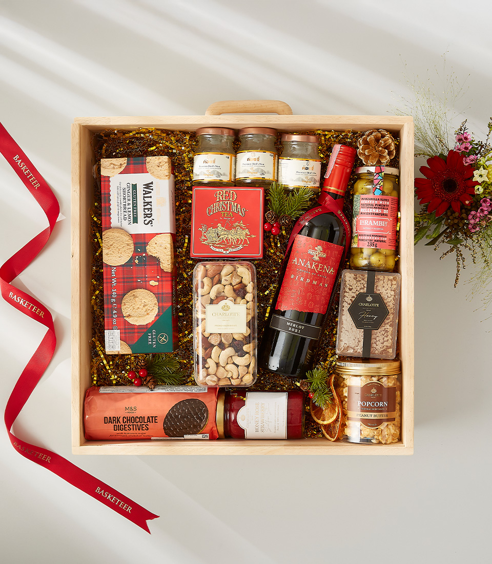 A luxurious Christmas gift basket filled with a bottle of red wine, assorted cookies, nuts, chocolates, and other festive goodies.