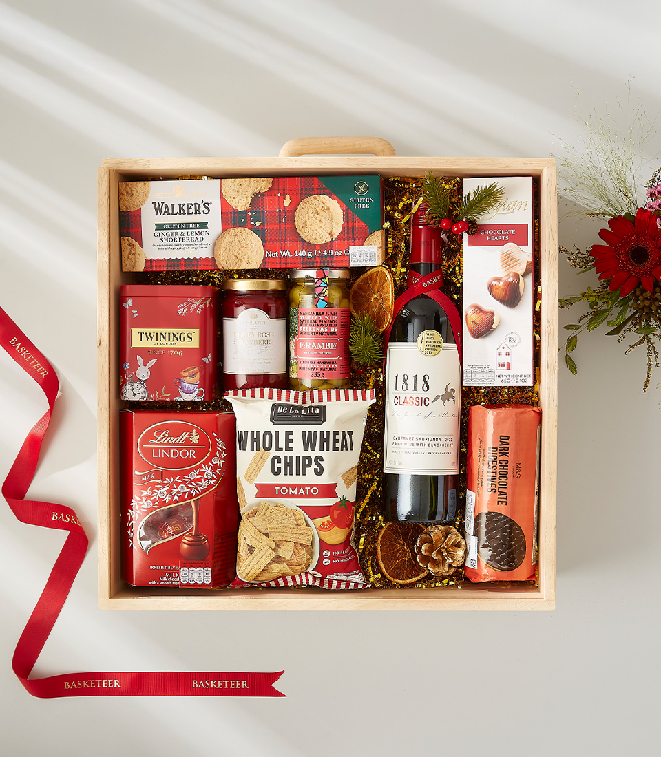 A luxurious Christmas gift basket filled with a bottle of wine, assorted cookies, nuts, chocolates, and other festive goodies.