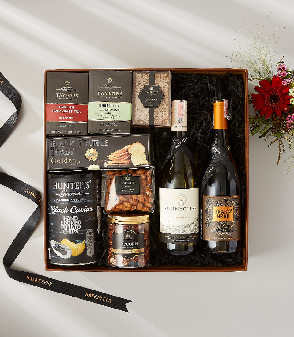 Festive gift hamper containing a bottle of wine, gourmet snacks, and Christmas decorations.