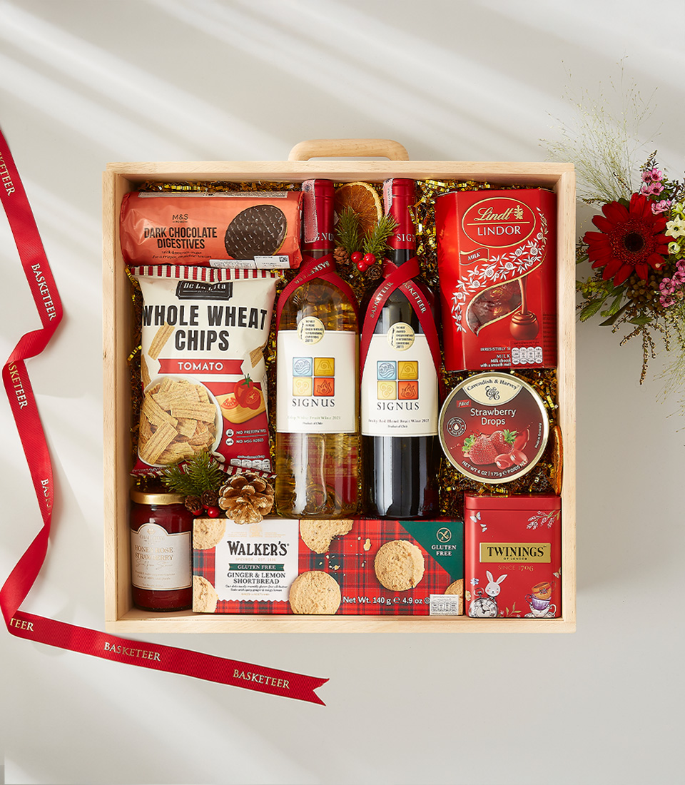 A wooden crate filled with a variety of Christmas treats, including a bottle of red wine, cookies, nuts, chocolates, and popcorn