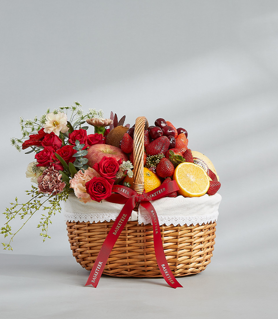 Romantic flower and fruit basket with fresh strawberries, cherries, pomegranate, citrus, and a bouquet of red and pink roses.